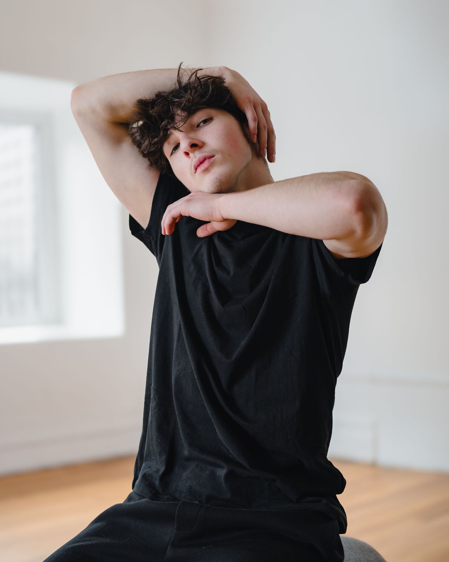Male dancer in black t-shirt seated mid-pose in bright dance studio by Bylitos Studio Michigan