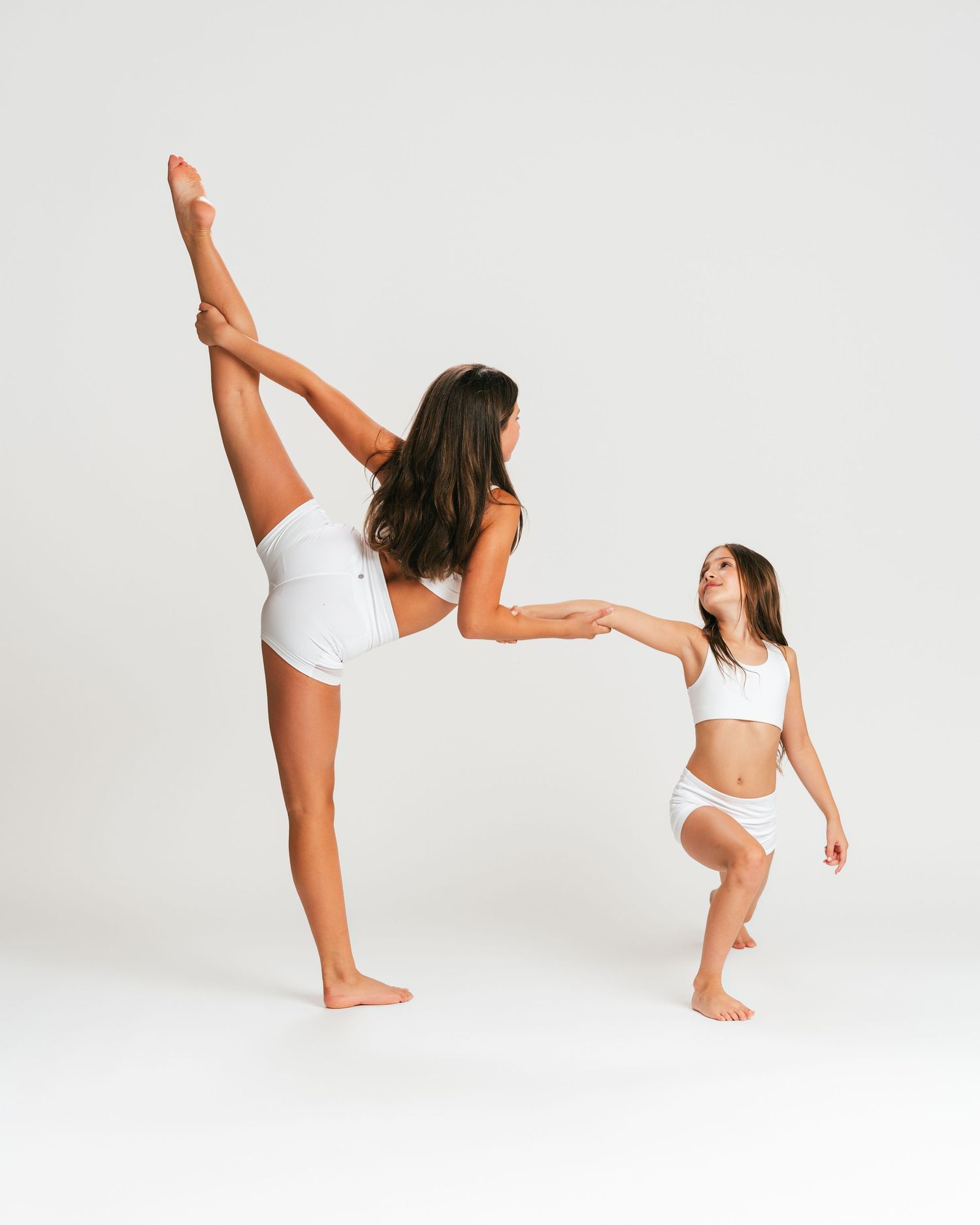 Adult and young dancer in white practicing a high kick together in studio editorial by Bylitos Studio Michigan