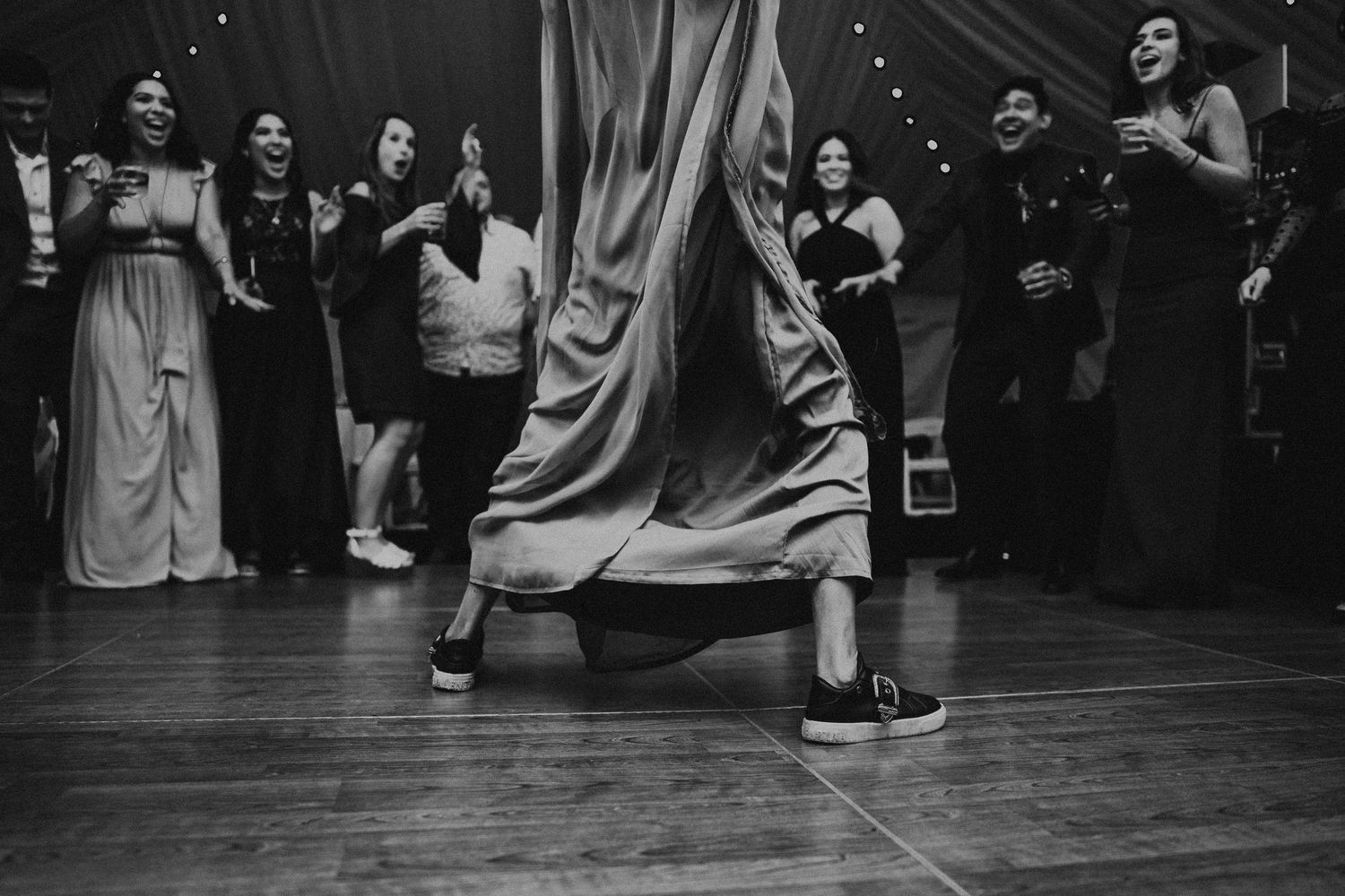 Black and white reception photo of guest dancing dramatically as crowd cheers by Bylitos Studio Michigan