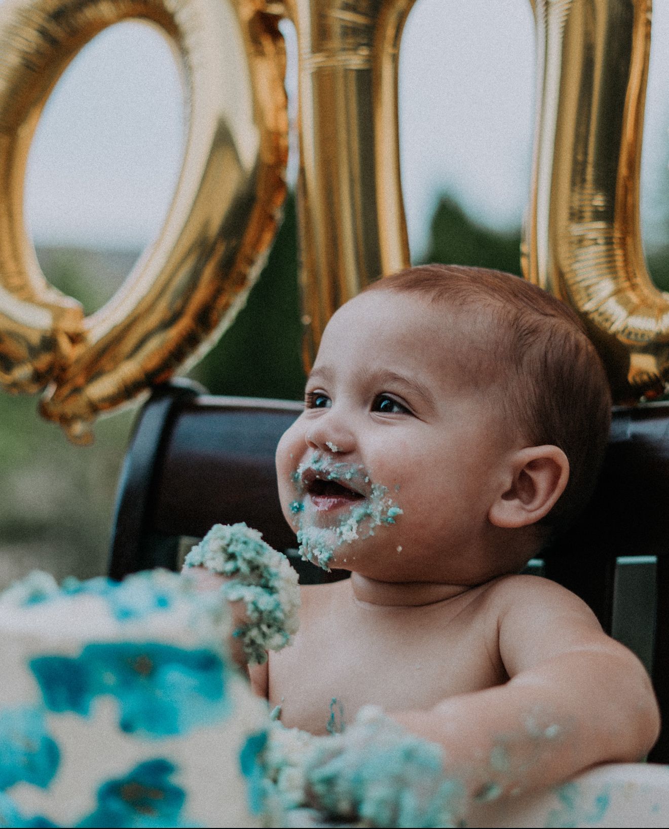 Baby enjoying first birthday cake smash with gold number one balloons by Bylitos Studio Michigan
