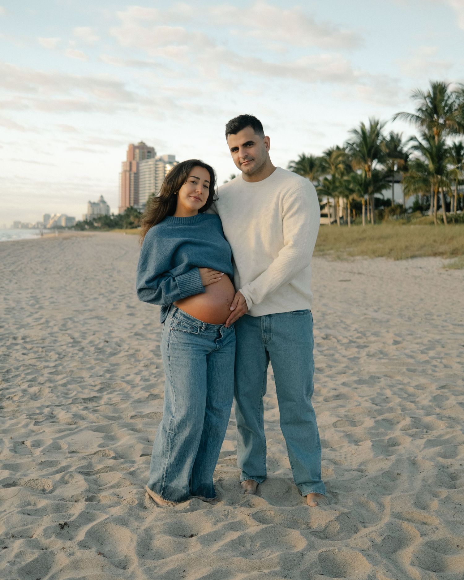 Expecting couple embracing at the beach during a maternity lifestyle session by Bylitos Studio Michigan