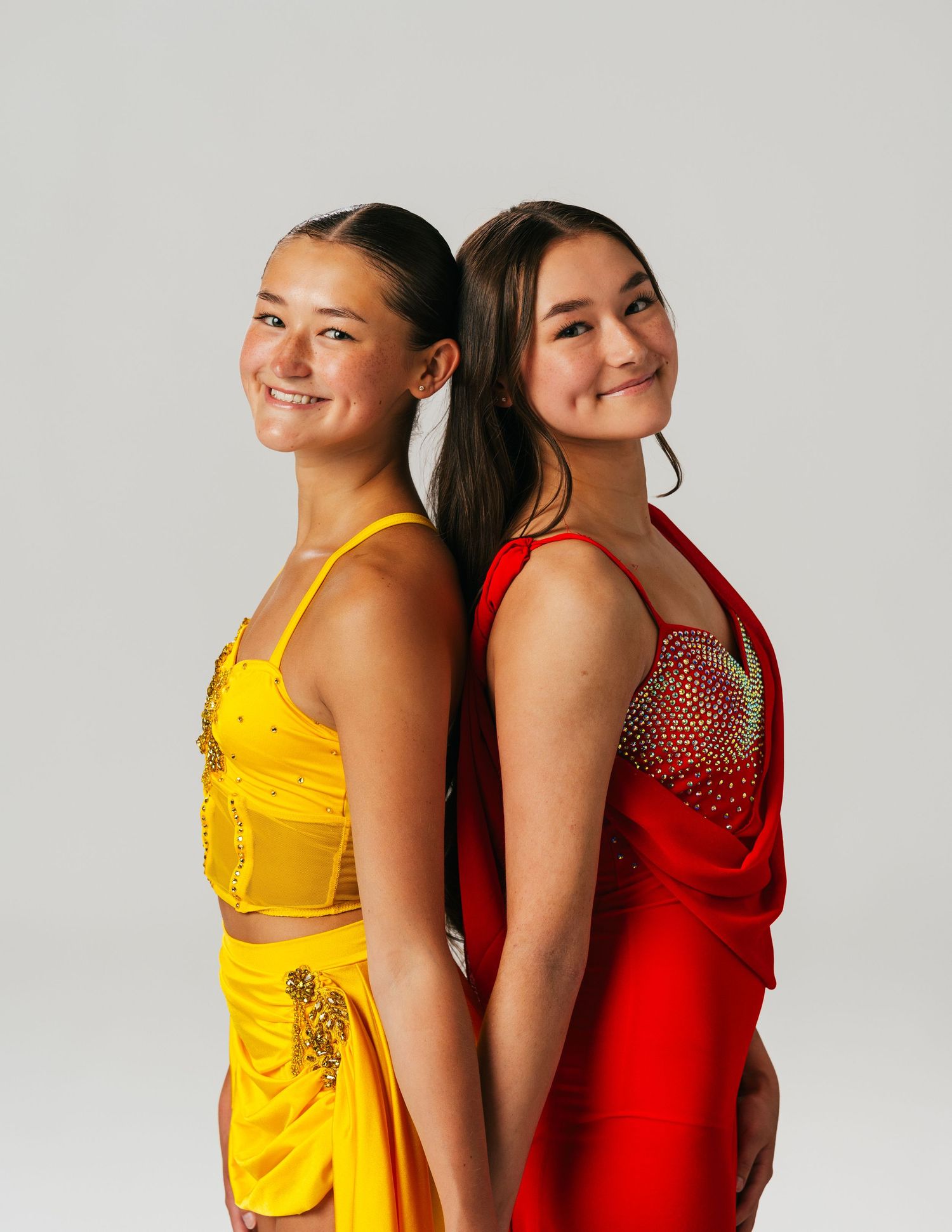 Two teen dancers in yellow and red dance costumes posing back-to-back by Bylitos Studio Michigan