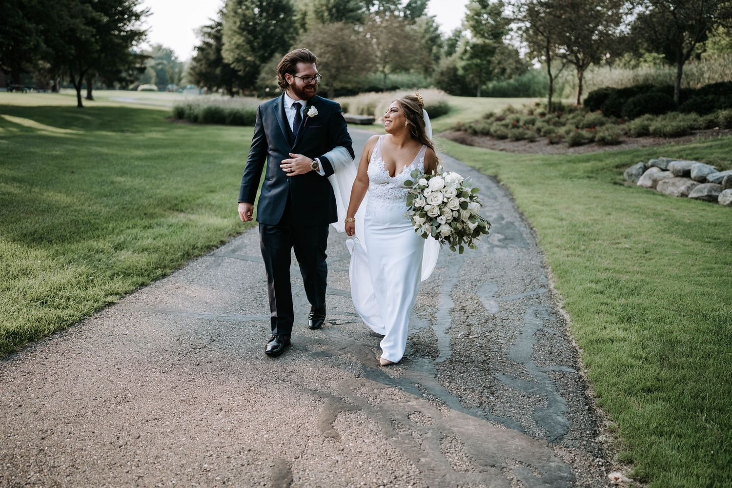 Bride and groom strolling together down a lush garden path on wedding day by Bylitos Studio Michigan