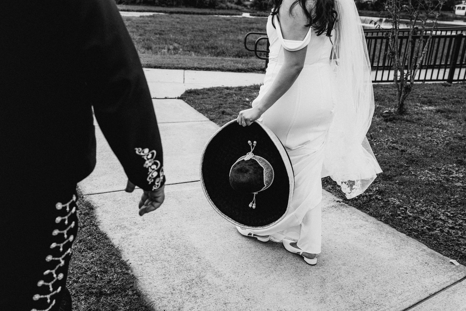 Black and white photo of couple walking with groom in mariachi suit and bride carrying a sombrero by Bylitos Studio Michigan