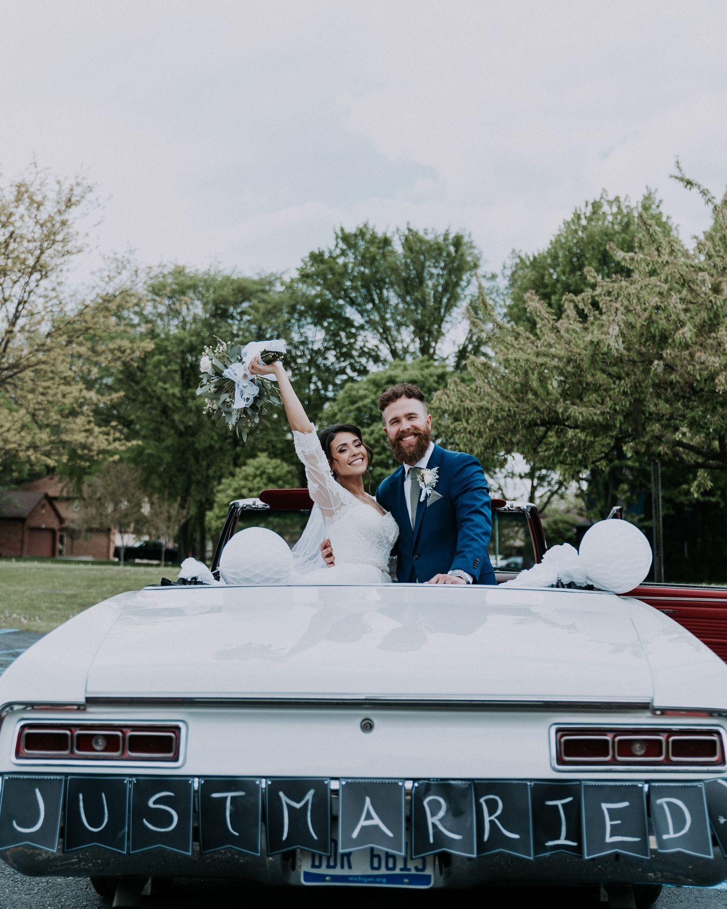 Newlyweds celebrating on a Just Married classic car with balloons during Michigan wedding by Bylitos Studio