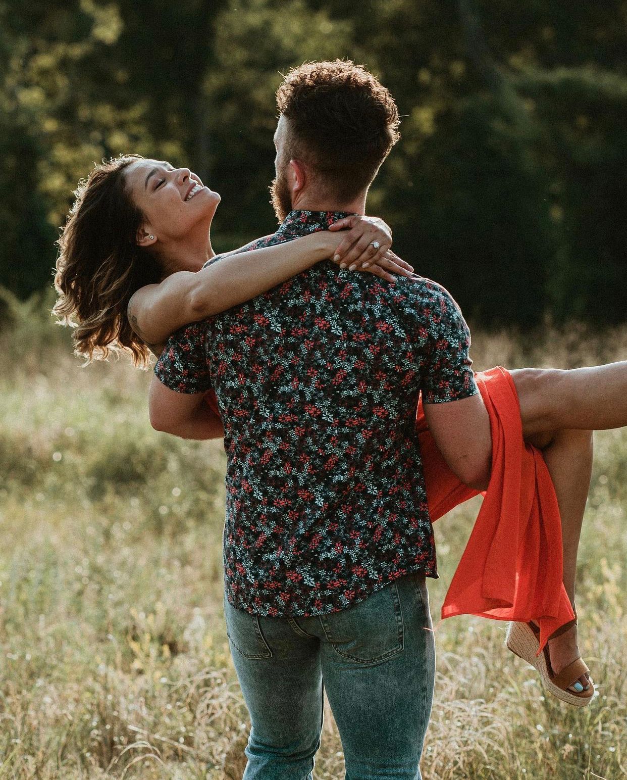 Man spinning woman in red dress in a wildflower field during engagement session by Bylitos Studio Michigan