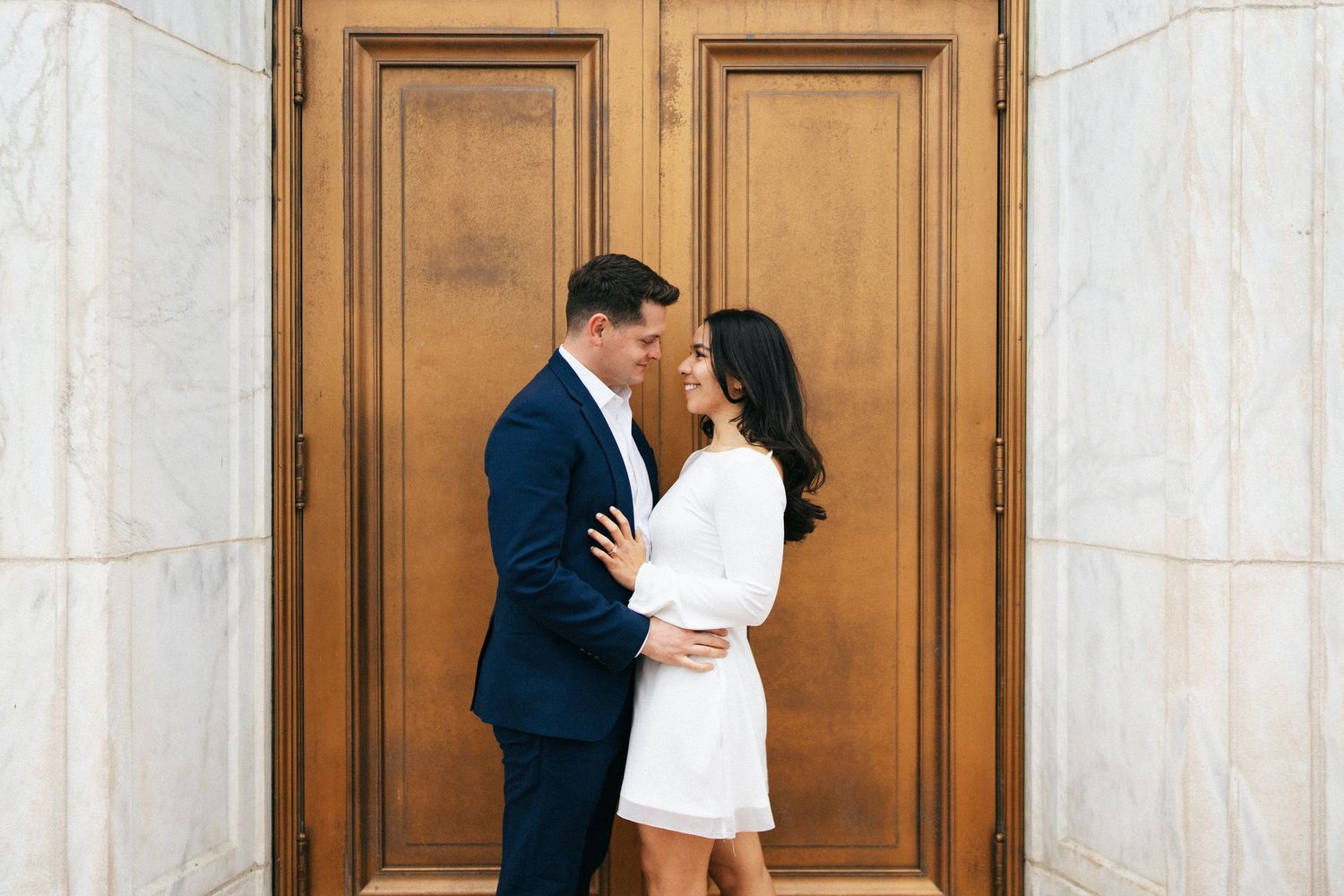 Engaged couple sharing a quiet moment in front of ornate wooden doors by Bylitos Studio Michigan