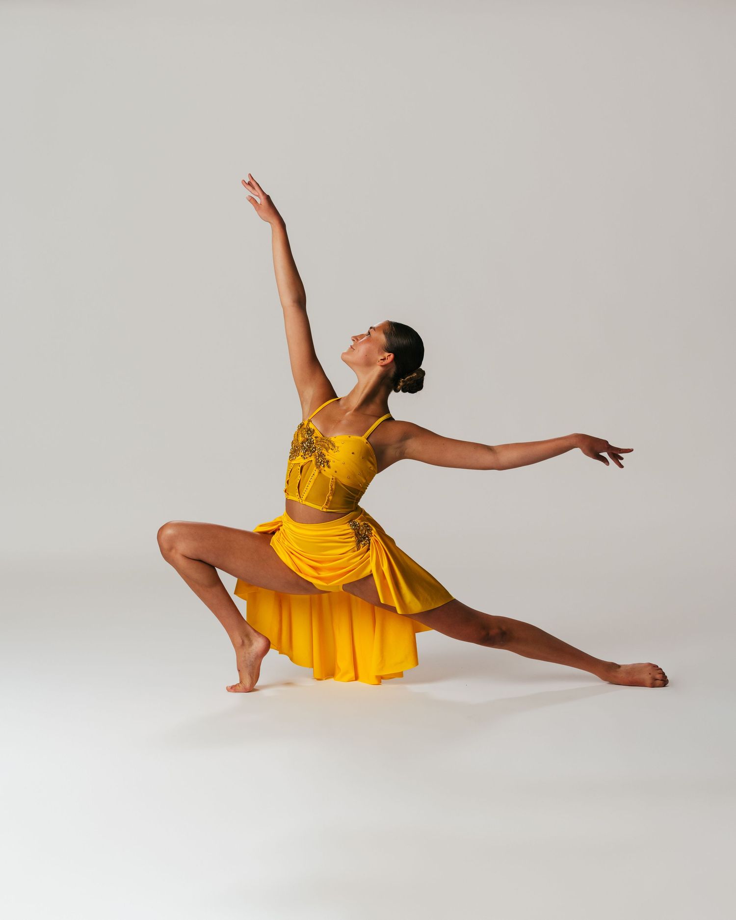 Dancer in gold yellow gown in graceful lunge with arm extended during editorial session by Bylitos Studio Michigan