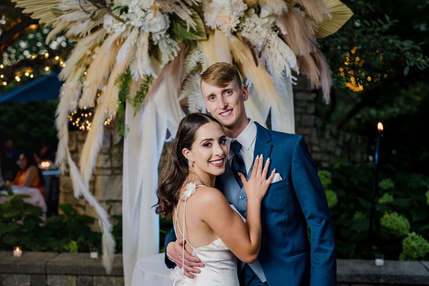 Michigan wedding couple posing under floral pampas grass arch at evening reception by Bylitos Studio Michigan