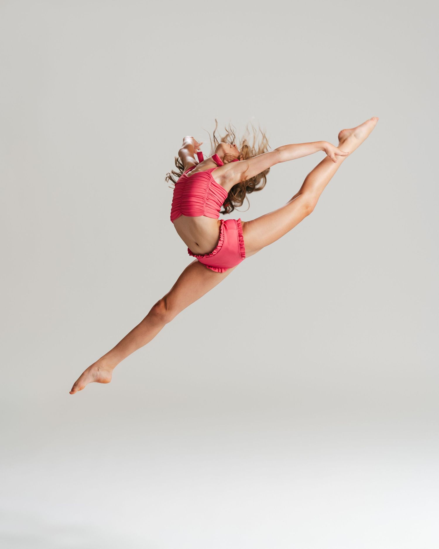 Young dancer in pink costume mid-leap with hair flying during studio editorial by Bylitos Studio Michigan