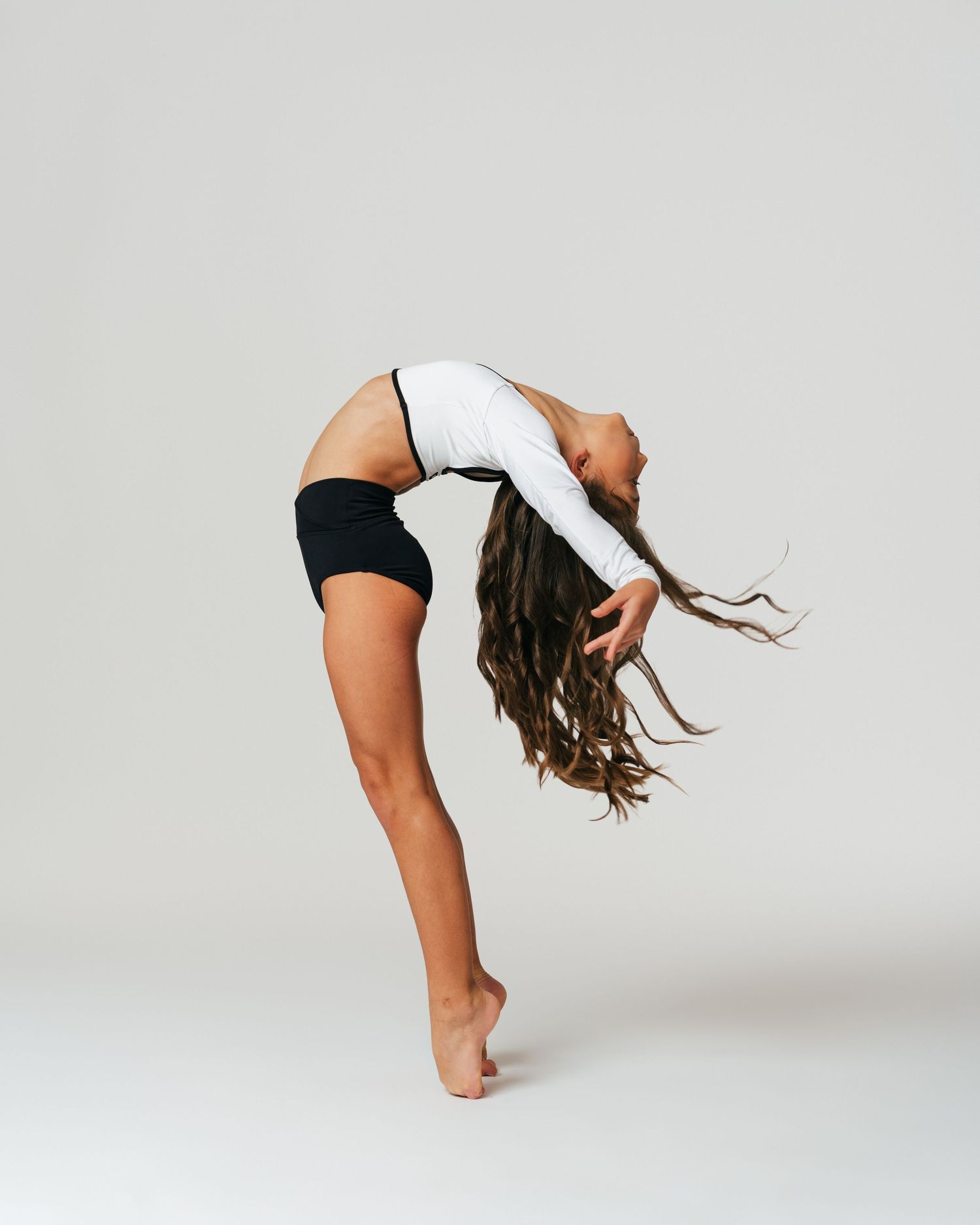 Dancer in white top dramatically arching back with hair flowing during editorial by Bylitos Studio Michigan