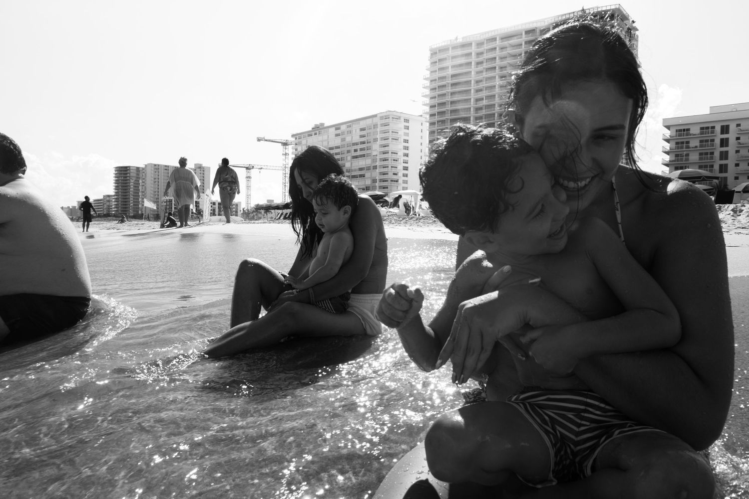 Black and white candid of mother hugging baby at the beach in a lifestyle session by Bylitos Studio Michigan
