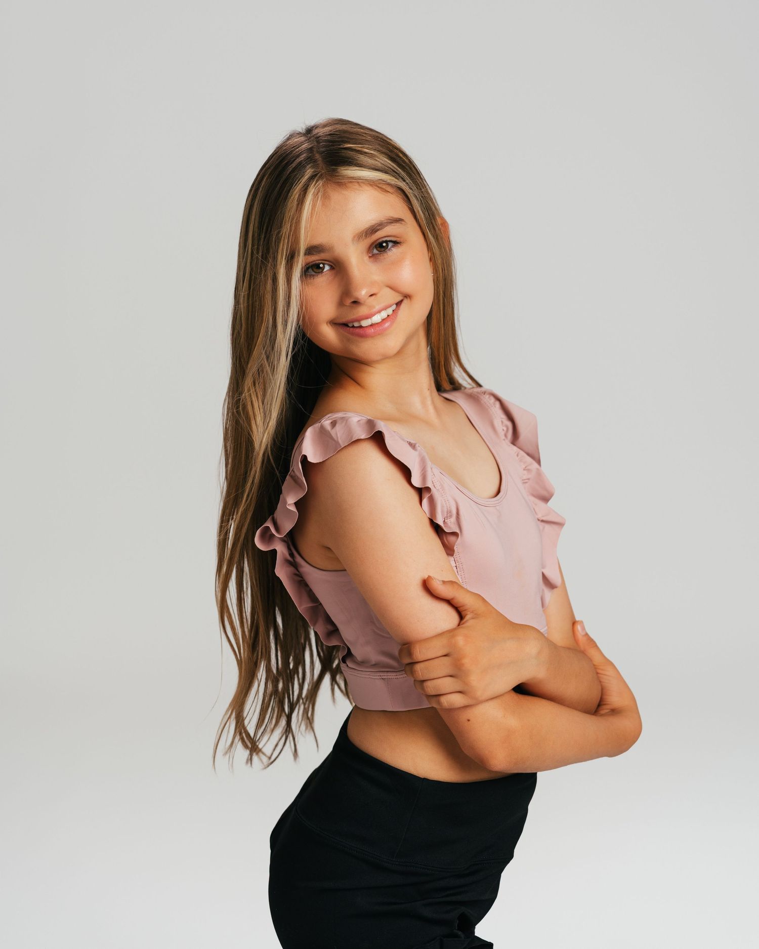 Young dancer in pink top with arms crossed smiling during studio portrait session by Bylitos Studio Michigan