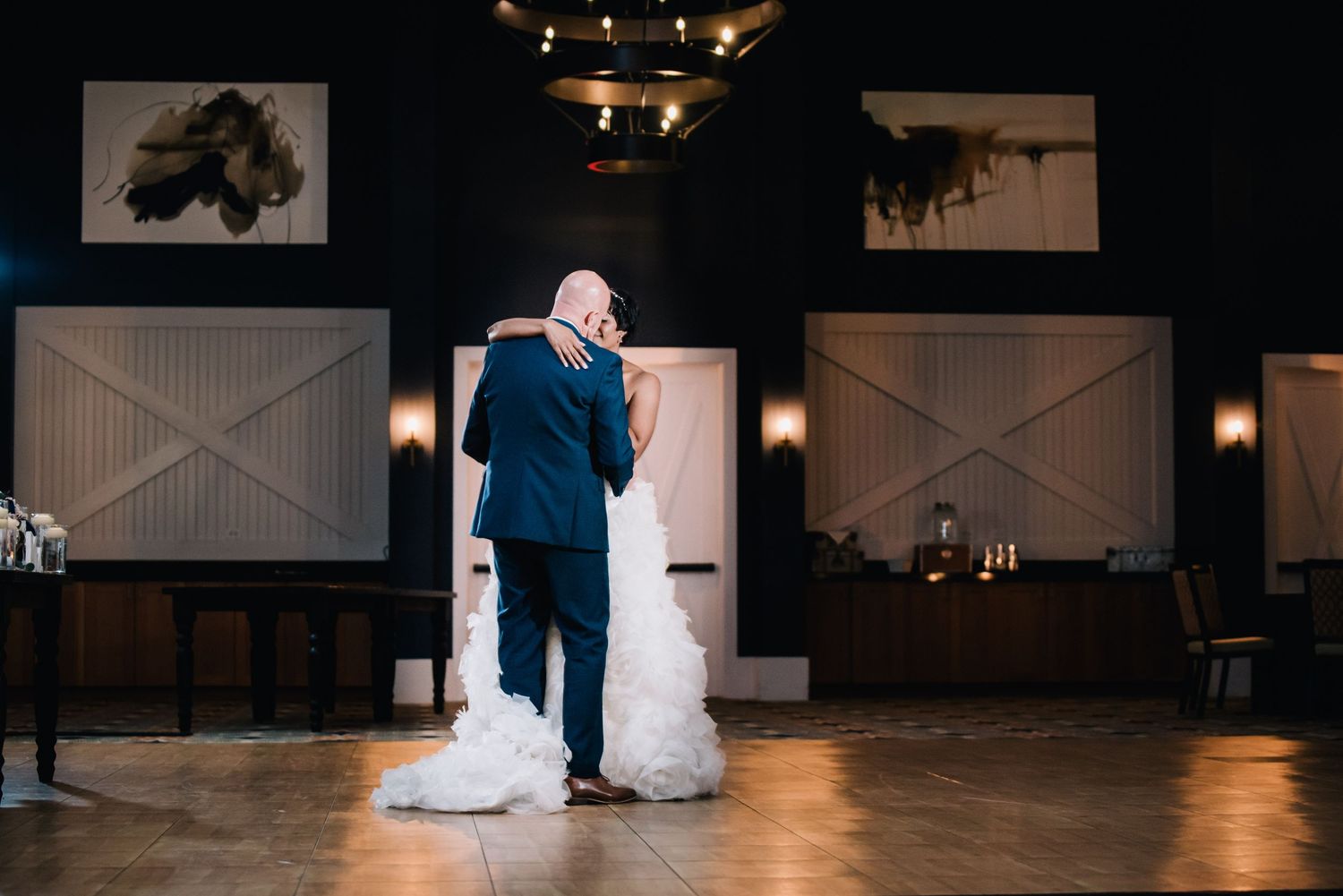 Couple embracing on dance floor in elegant reception venue with rustic barn-style decor.