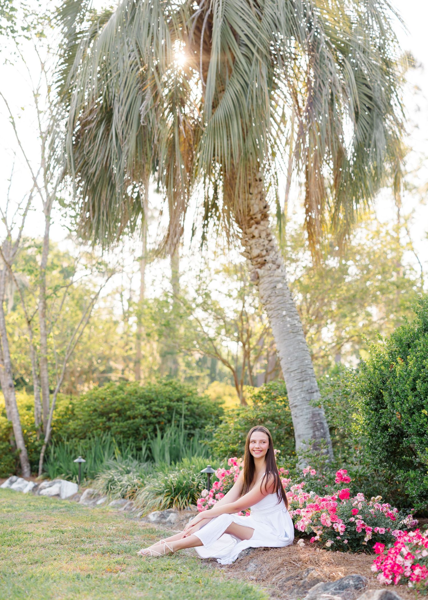 A scenic outdoor portrait session featuring palm trees, pink flowers and a dreamy sunlit garden setting.