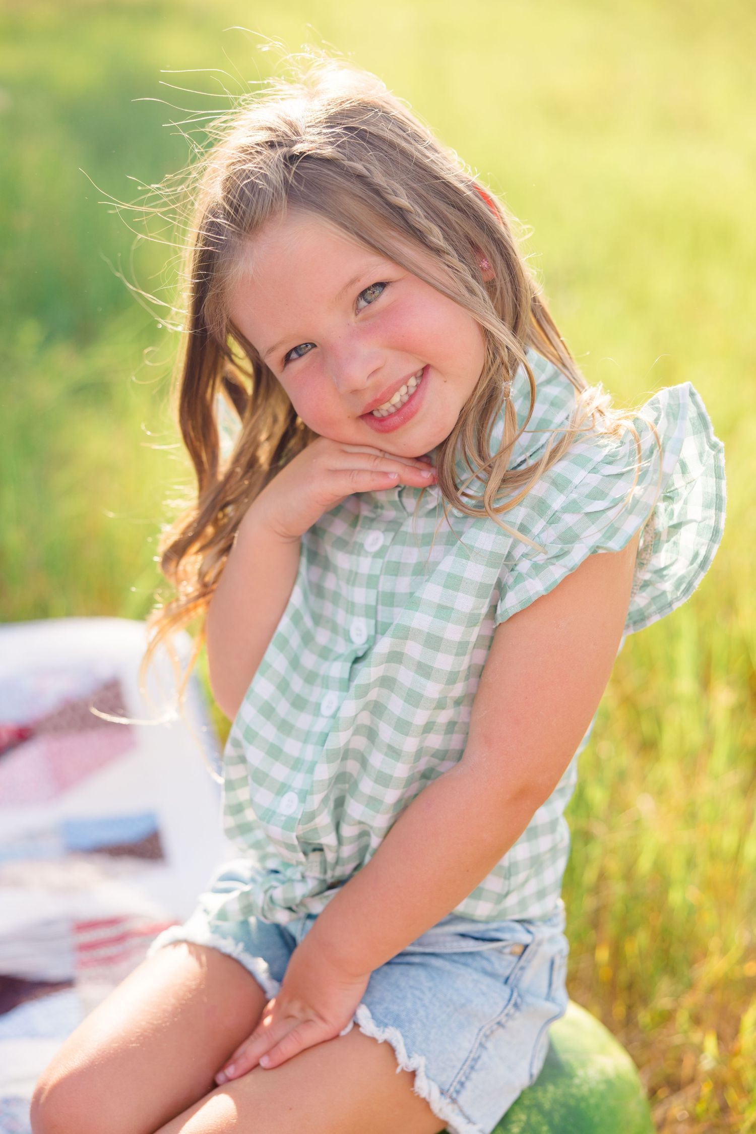 A child in a mint gingham top poses playfully in golden sunlit grass.