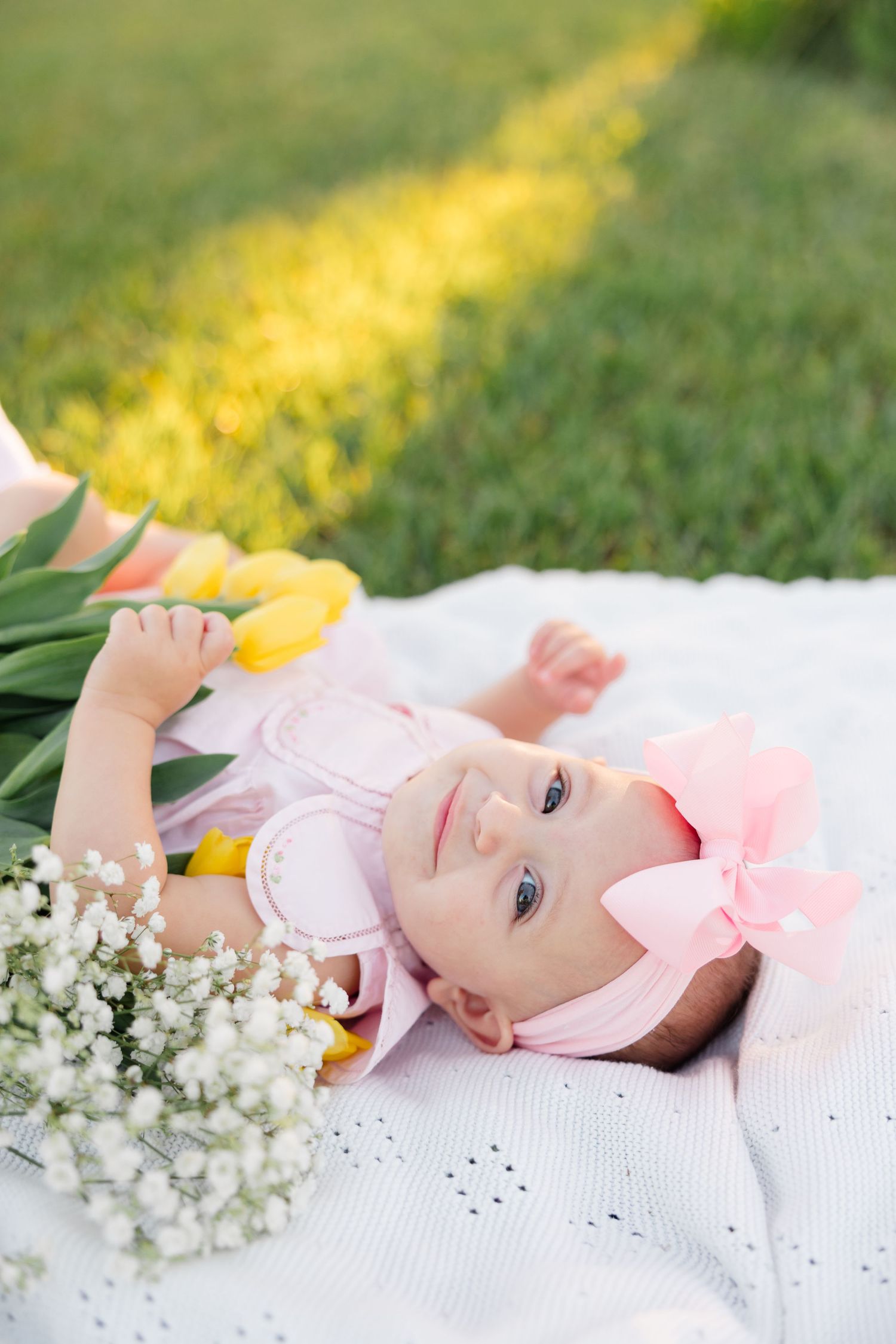 A series of photos showing a baby in pink clothing lying on white fabric with white baby's breath flowers.