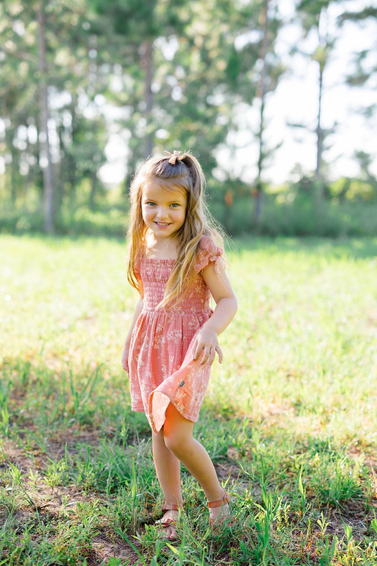 Young girl in pink dress twirling playfully in a sunny meadow.