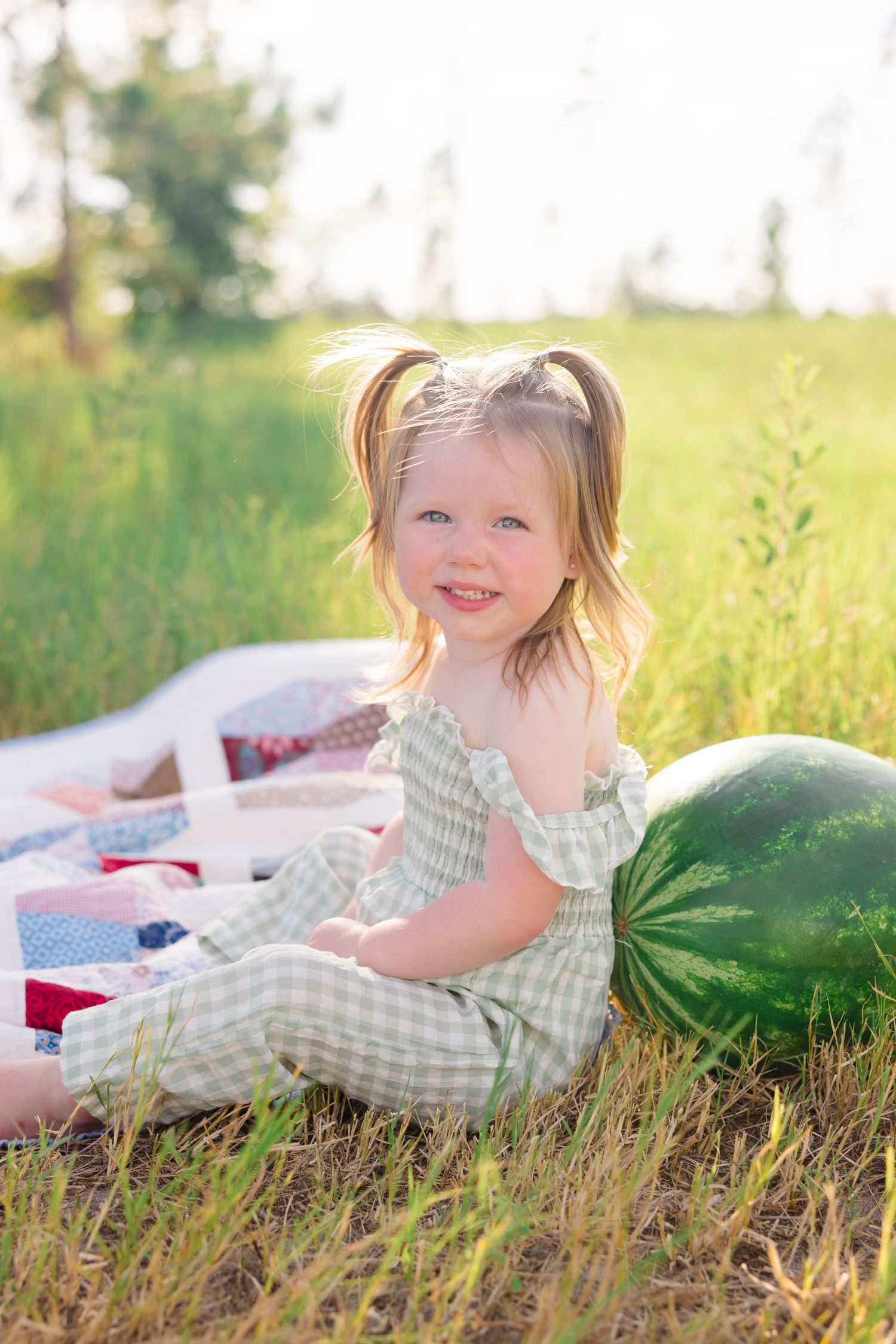 A child lies on a blanket next to a watermelon in summer grass during golden hour.