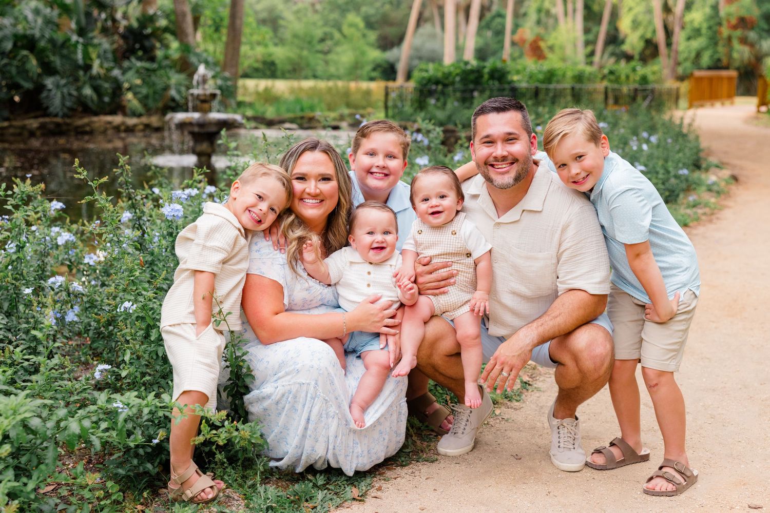 Family wearing white outfits poses candidly together outdoors for professional portraits in a garden setting.