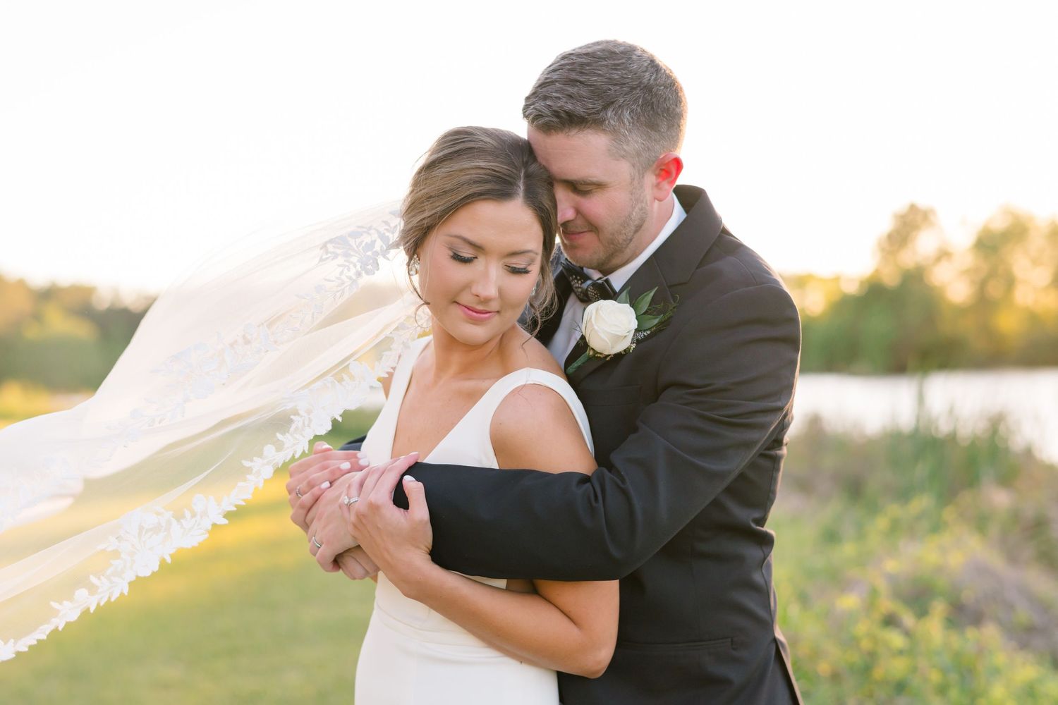 Intimate wedding couple embraces during golden hour sunset by a lake.