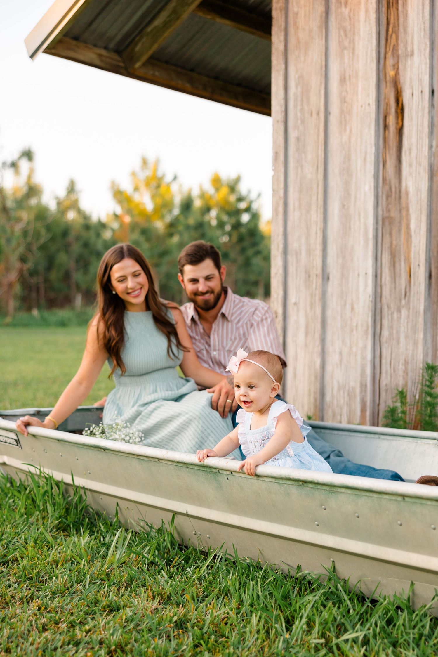 A family lies together on a rustic wooden porch surrounded by grass during a warm outdoor photo session.