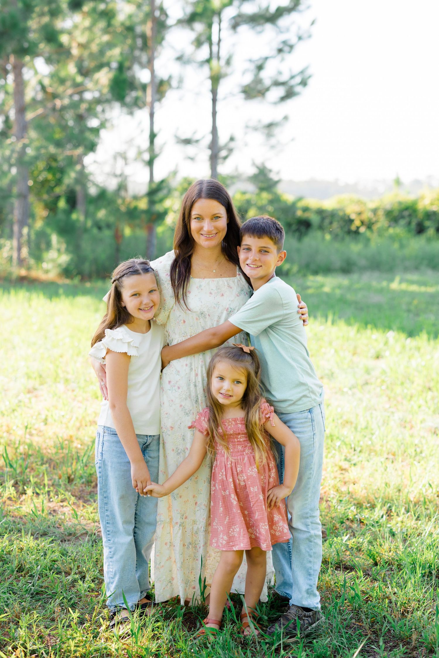 Family portrait in a sunny meadow with pine trees in the background.