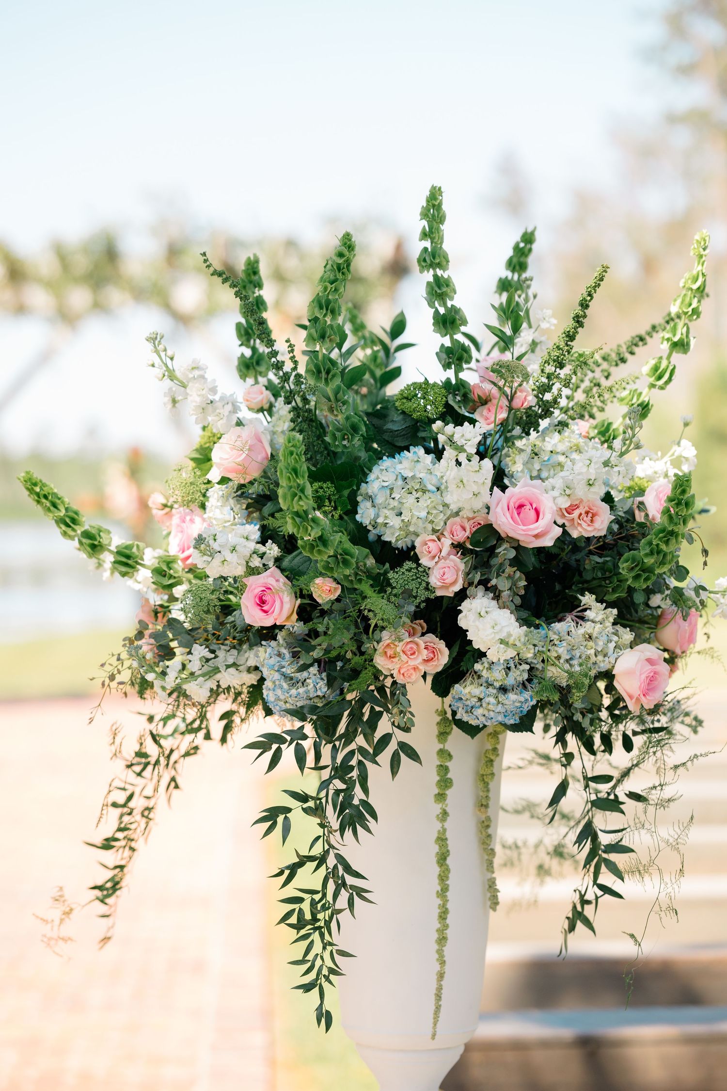 Elegant floral arrangement with pink roses, white hydrangeas and cascading greenery on a soft blurred background.