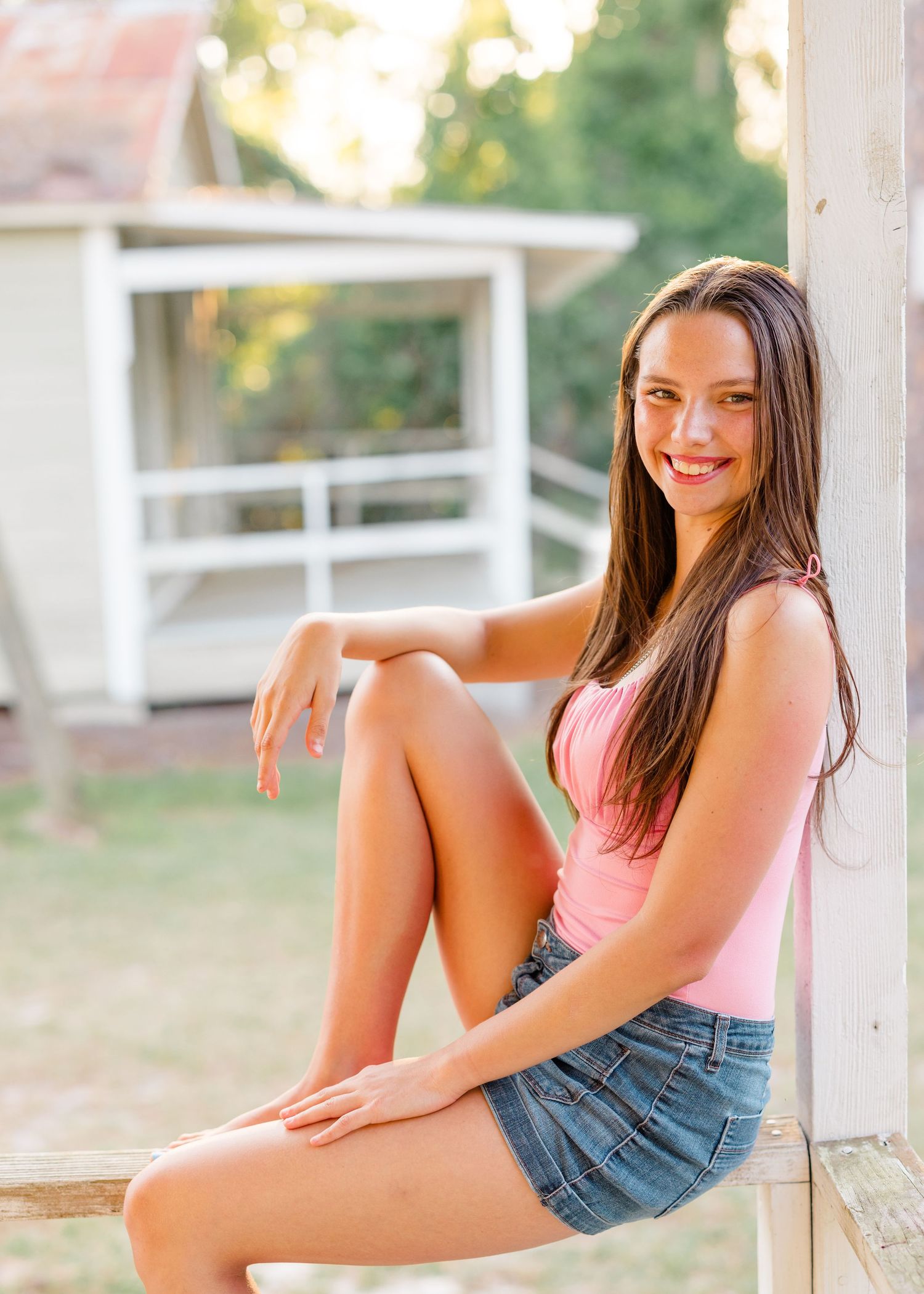 Summer portrait session on a white porch featuring casual denim and pink tank top outfit.