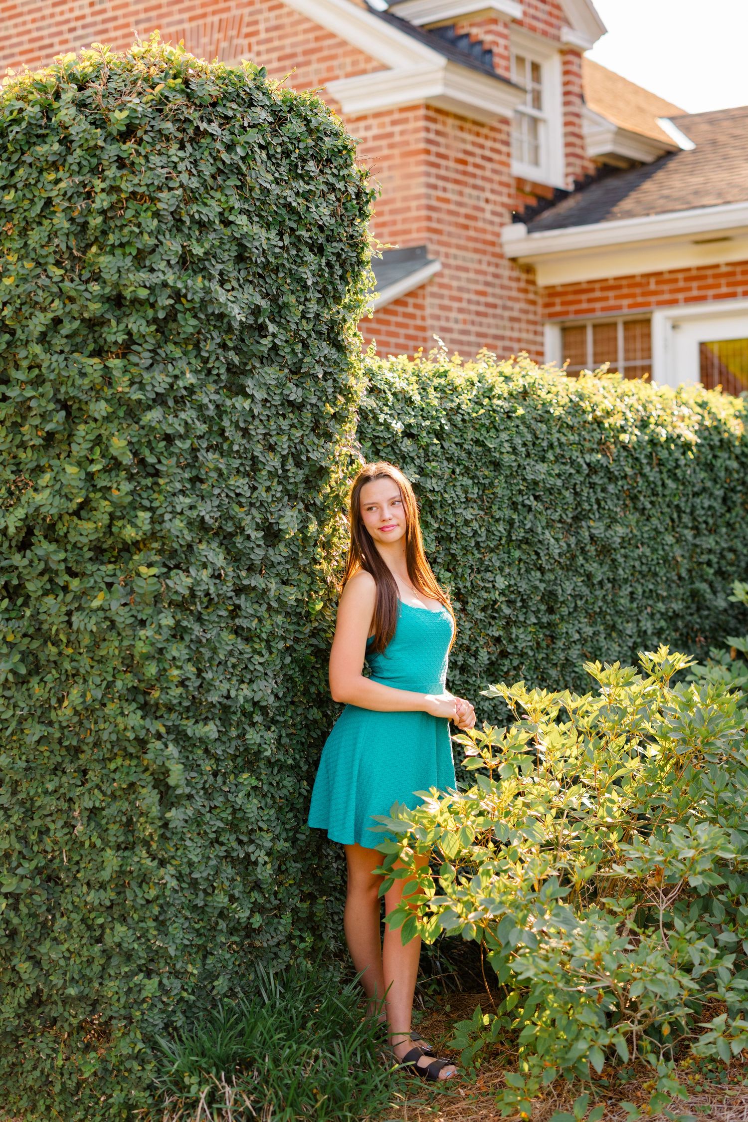 Portrait session against brick wall and green hedge wearing teal dress.
