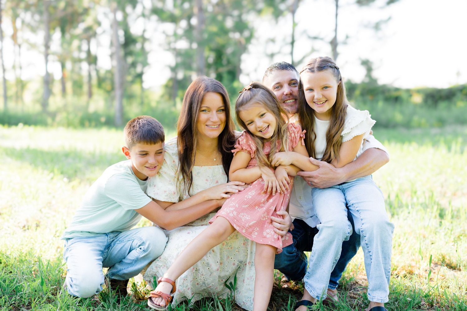 A happy family group shares laughs and hugs while posing in a sunlit field.