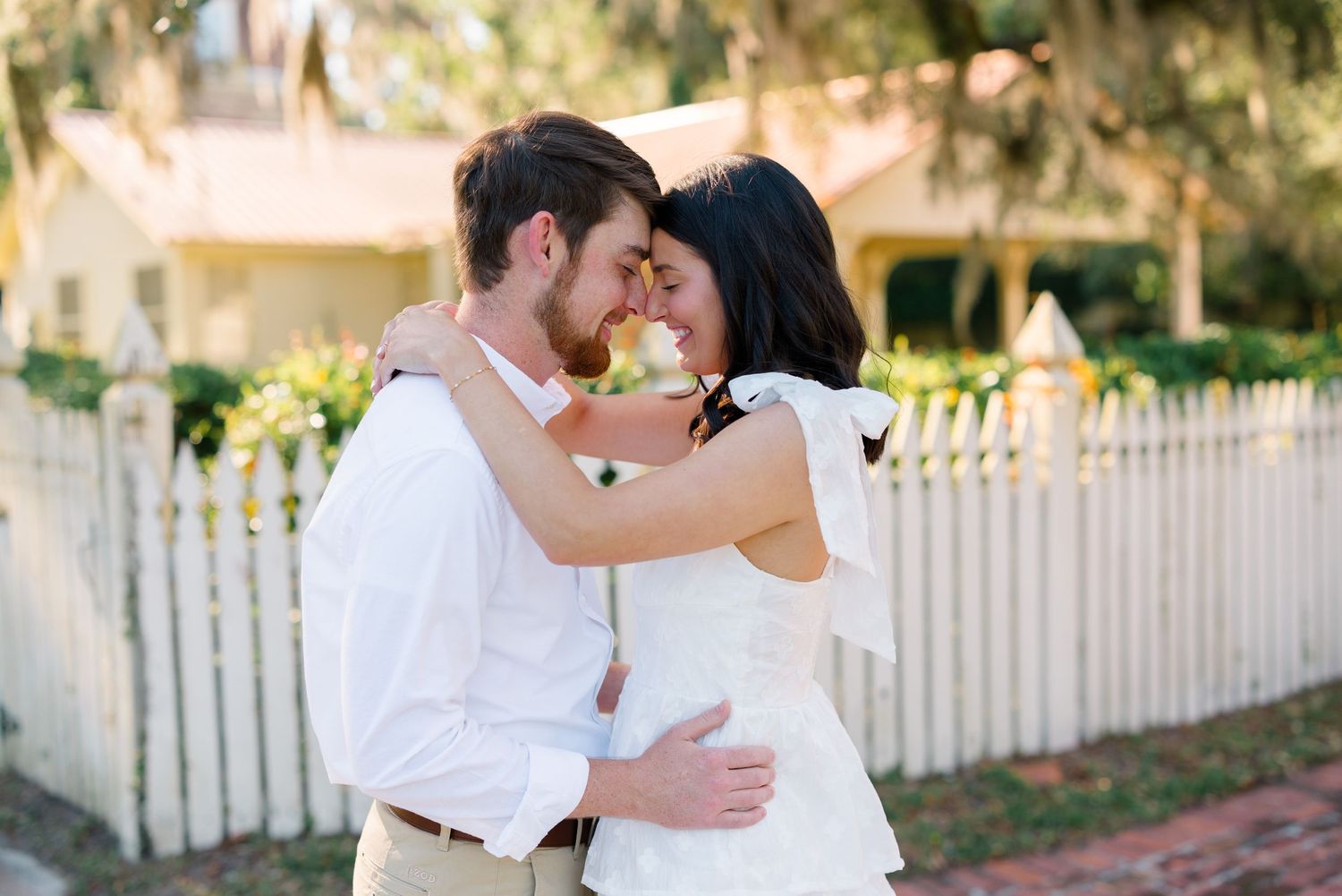 A couple shares a romantic moment outdoors in white and khaki outfits.