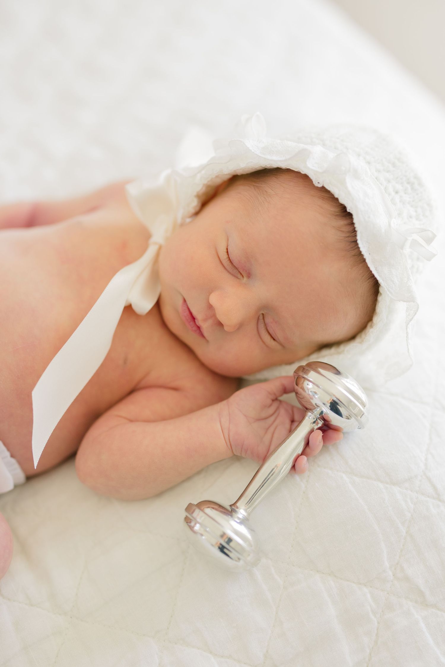 Sleeping newborn baby wrapped in soft white lace blanket holding small glass bottle in peaceful pose.