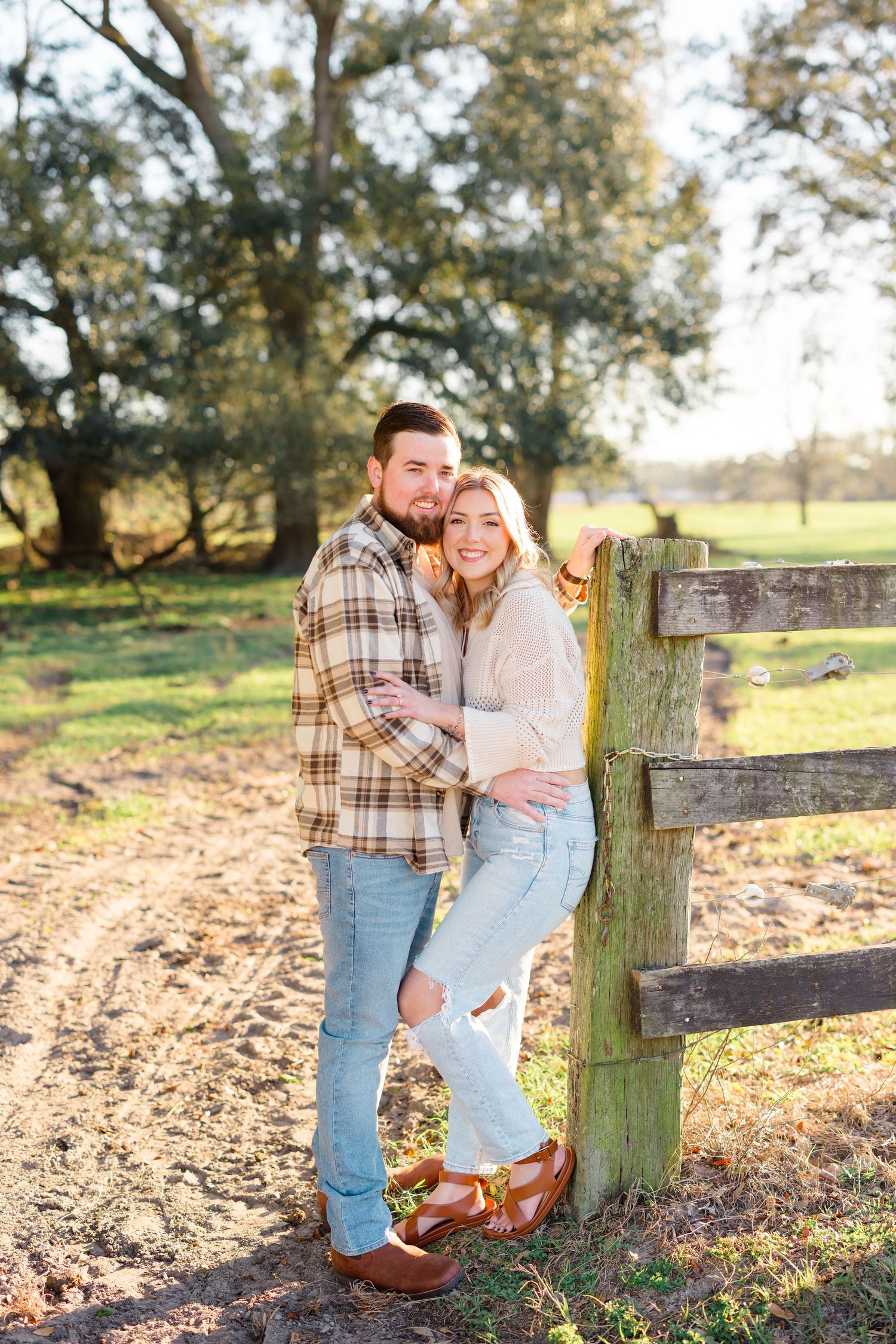 Couple embracing by a wooden fence post in an autumn field during golden hour.