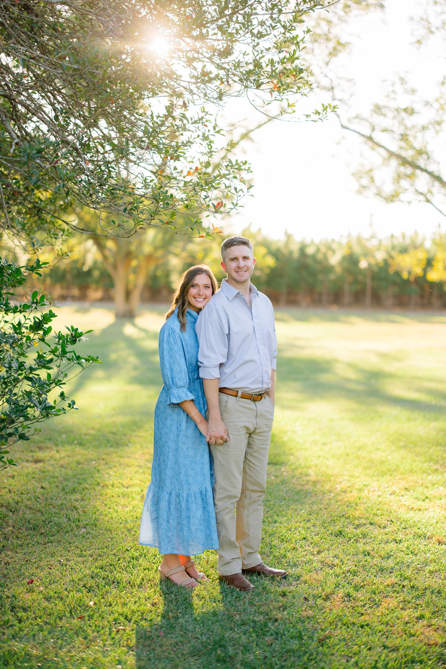 A couple stands together in a sunlit orchard during golden hour, sharing intimate moments in nature.