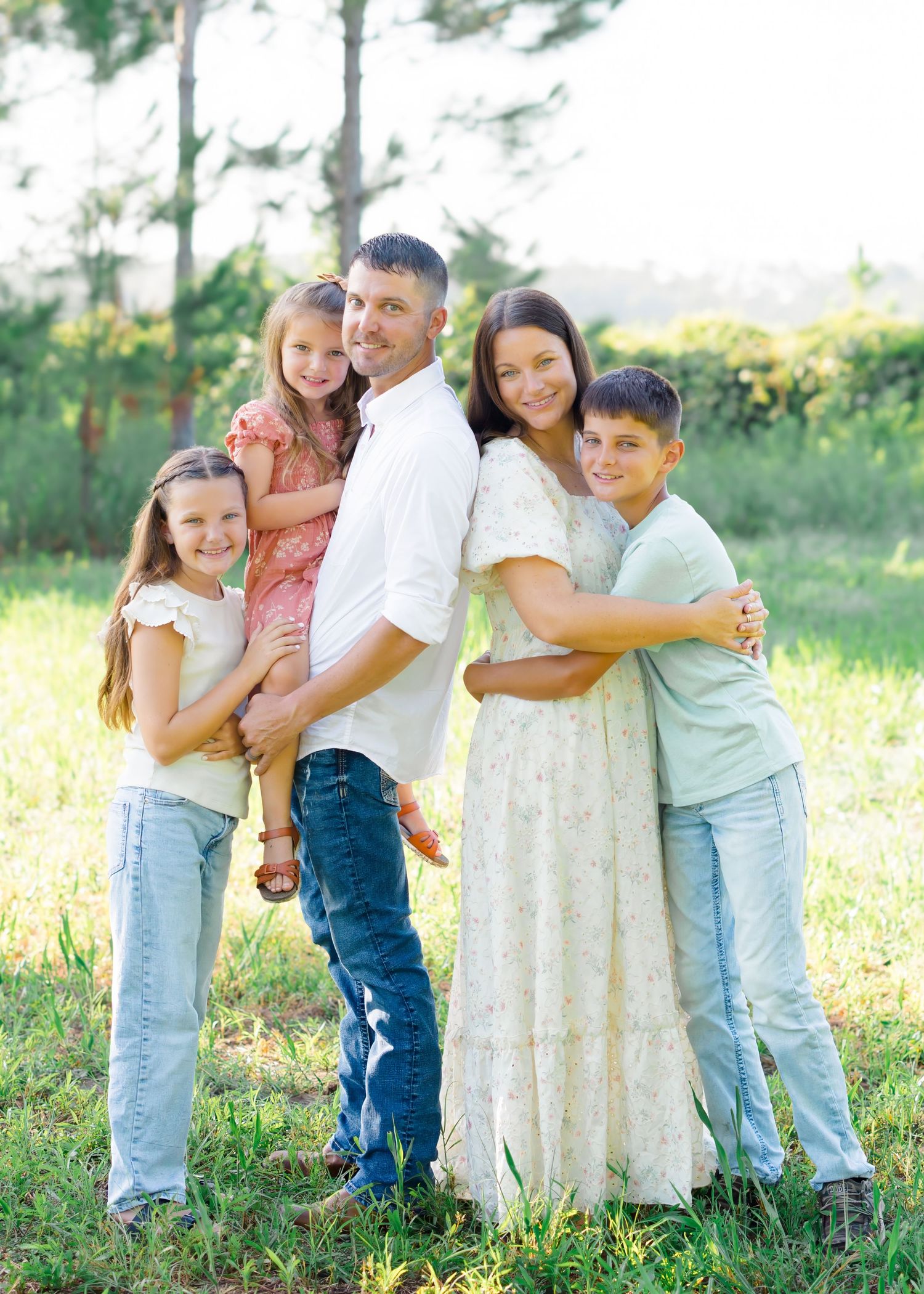 A family of five poses together outdoors in coordinated casual outfits.