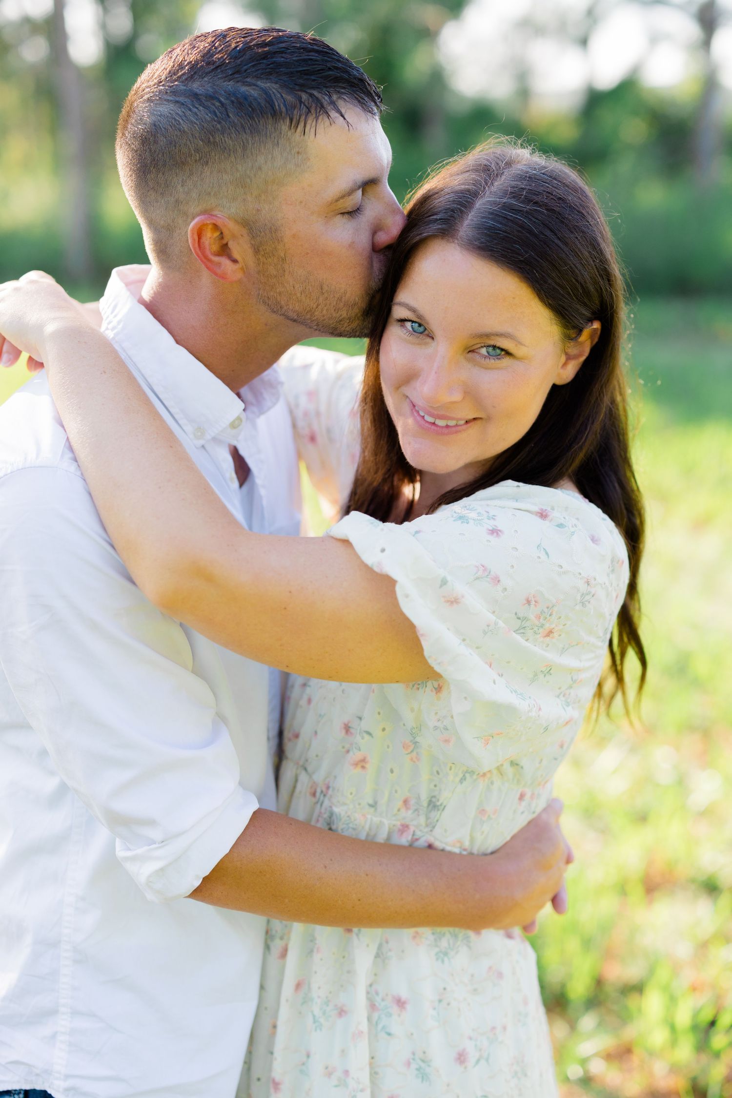 Romantic couple embracing outdoors in a scenic natural setting with soft lighting and greenery.