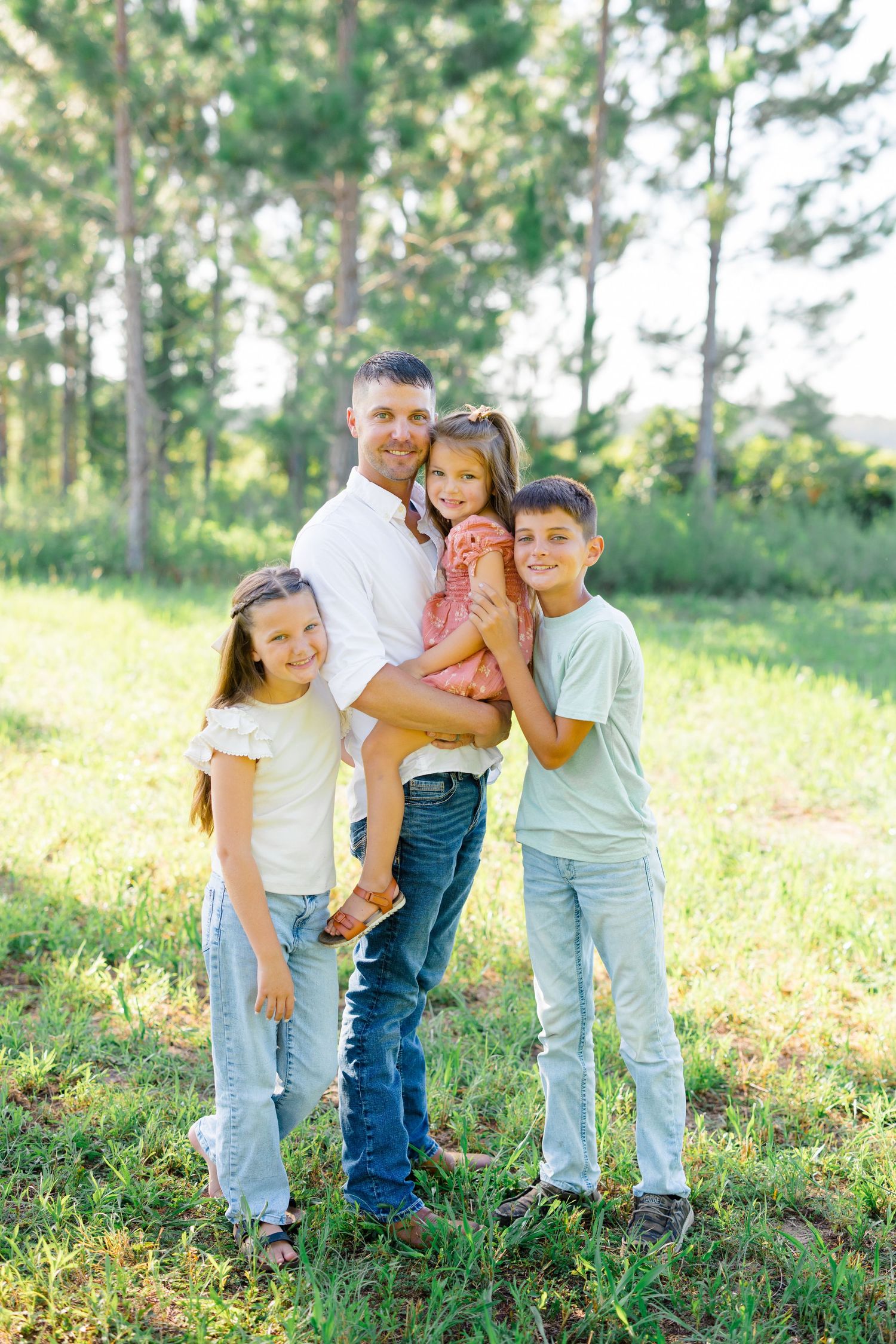 Family group hug outdoors with pine trees and natural lighting.