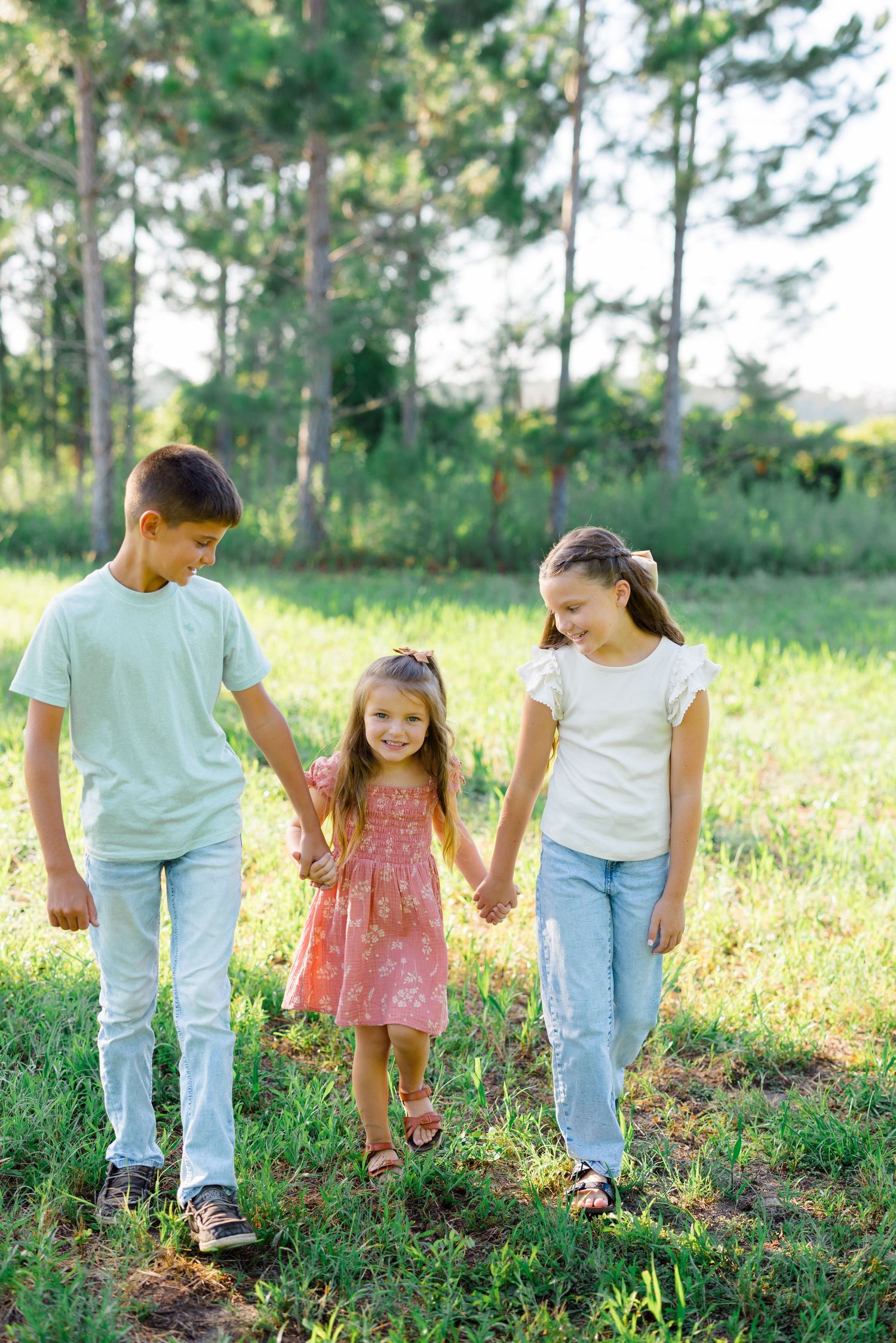 Family members walk together through tall grass in a sun-dappled outdoor setting.