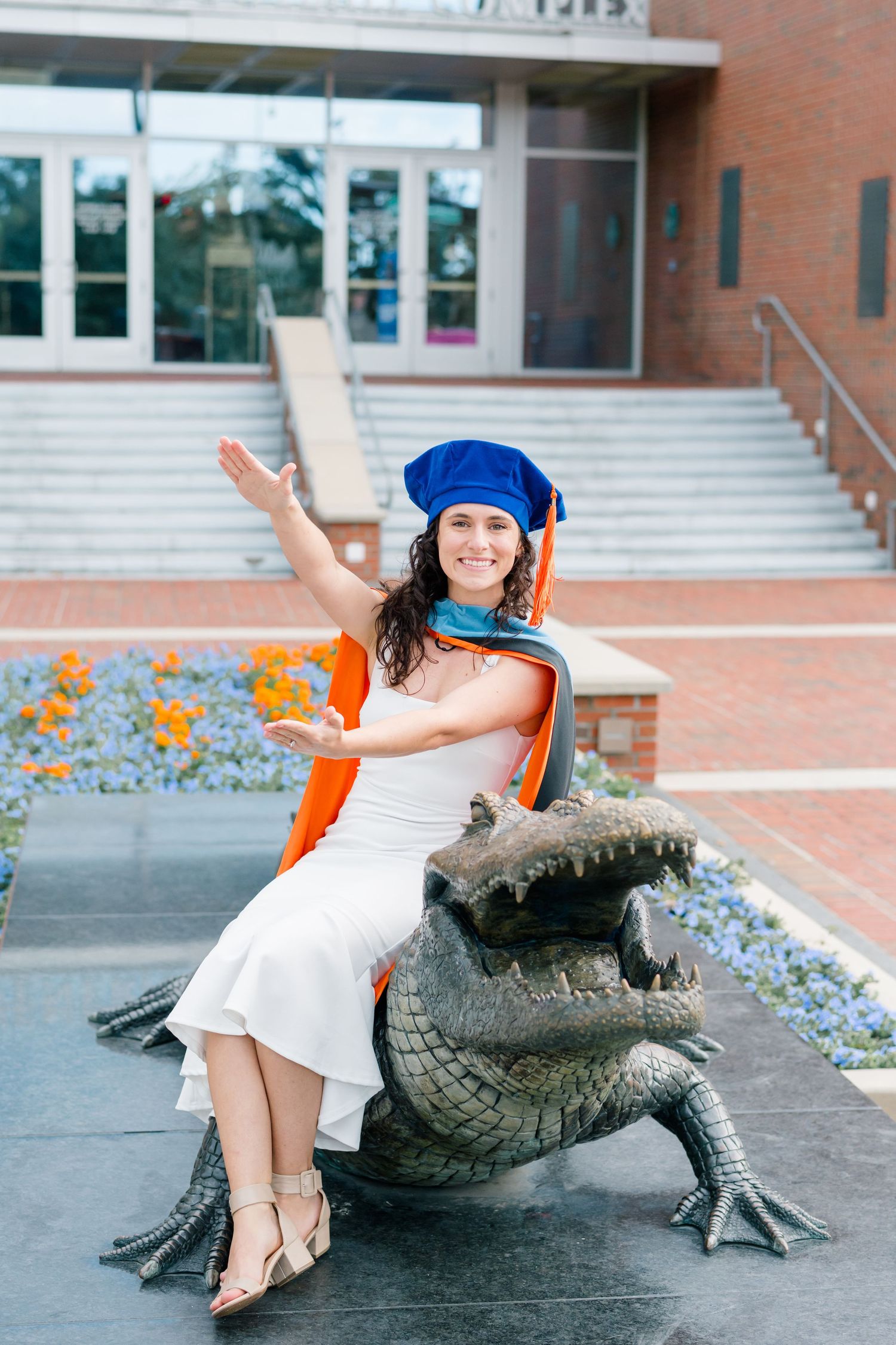 A series of playful poses with an alligator statue on campus steps surrounded by orange flowers.