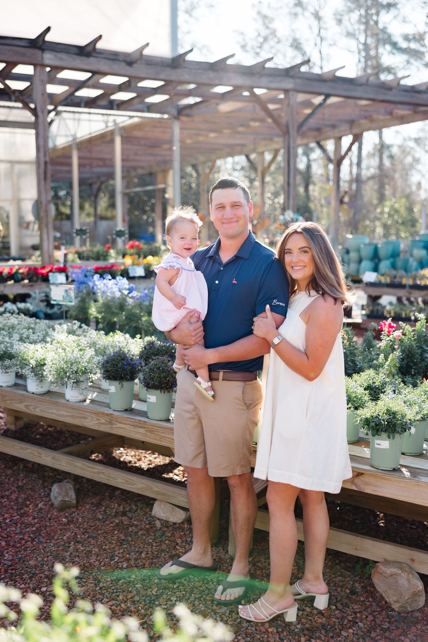 Family poses together at garden center surrounded by potted flowers and plants.