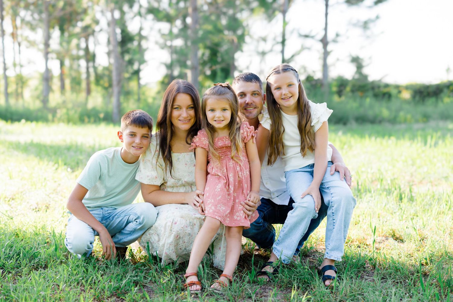 Family members share candid moments together while sitting in a grassy outdoor setting.
