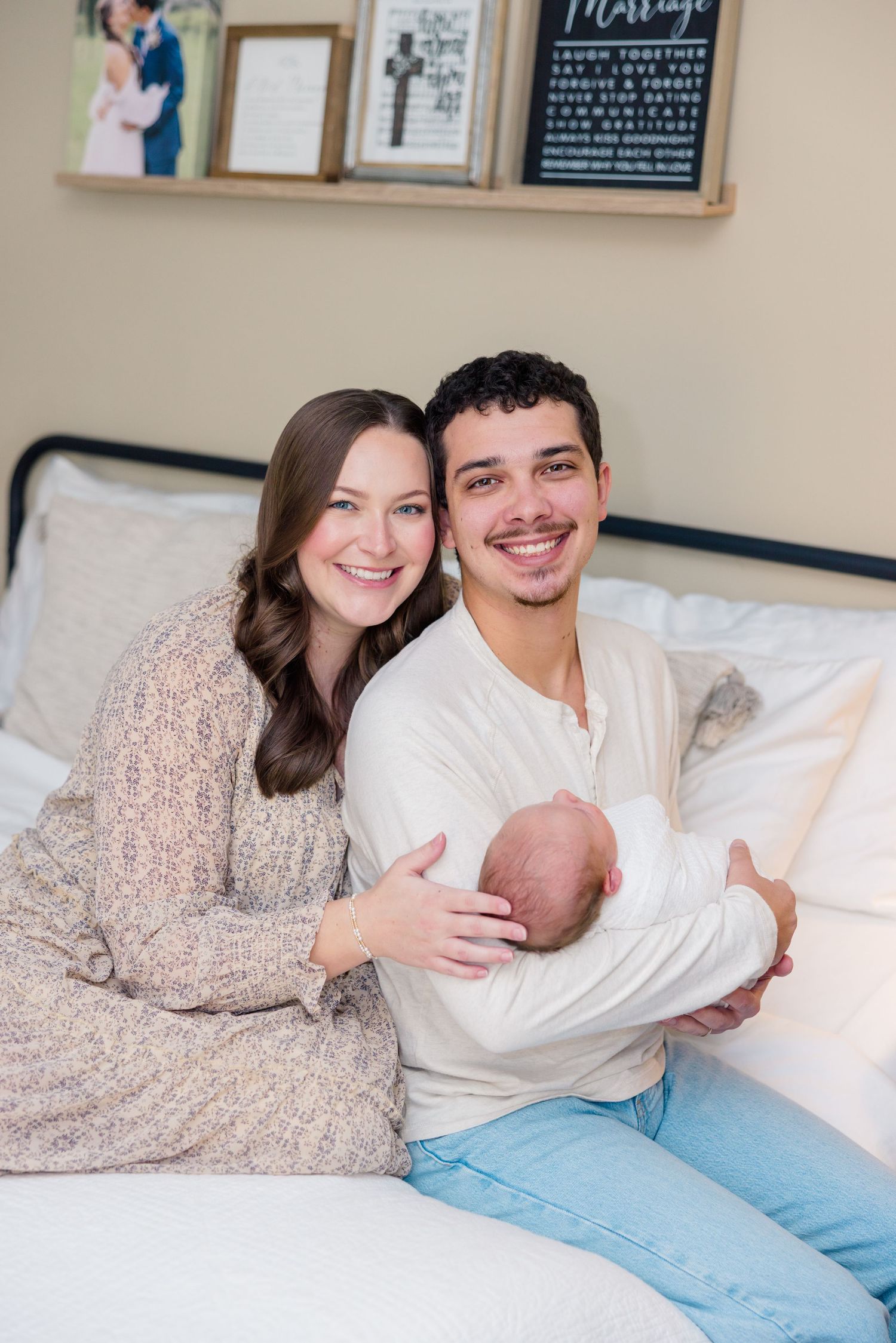 A couple lying together on a white bed with decorative wall art in the background.