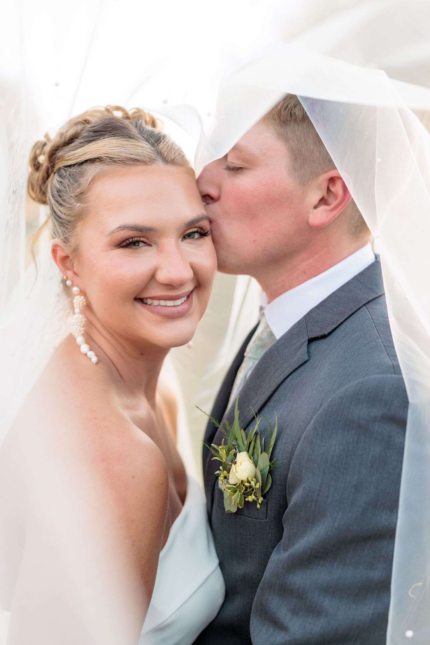 A romantic wedding moment captured as a groom in gray suit kisses his bride under soft lighting.