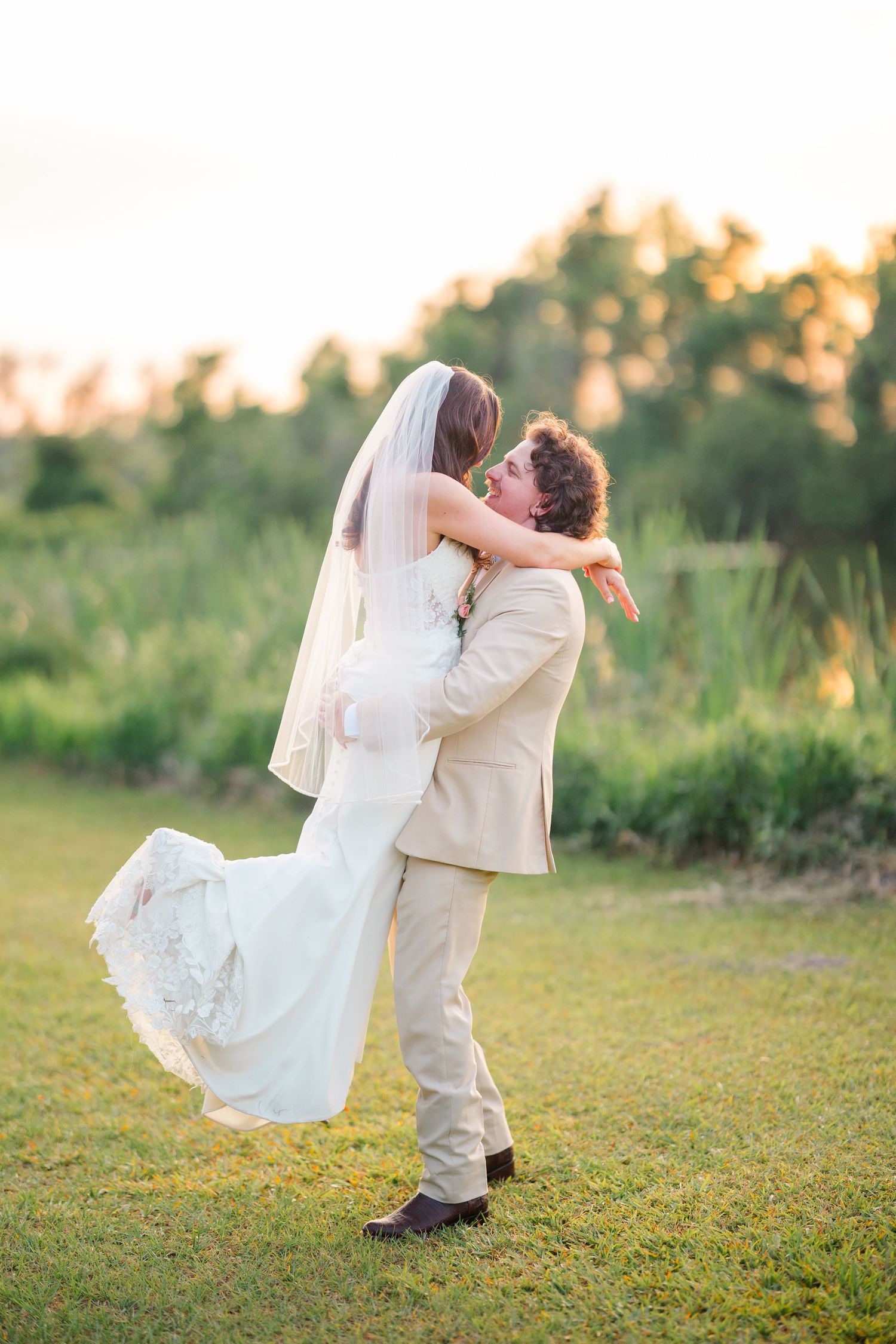 A romantic sunset wedding photo shows a couple embracing in a field as the groom lifts his bride in her flowing white dress.