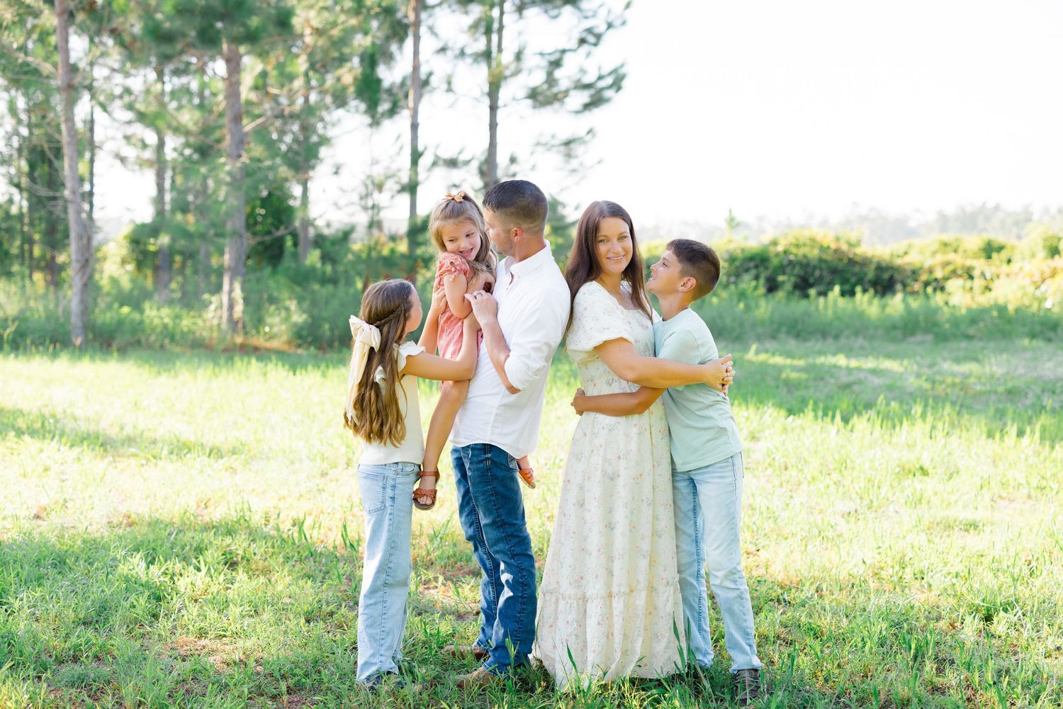 Family of four sharing a tender moment together in a sunny outdoor setting.