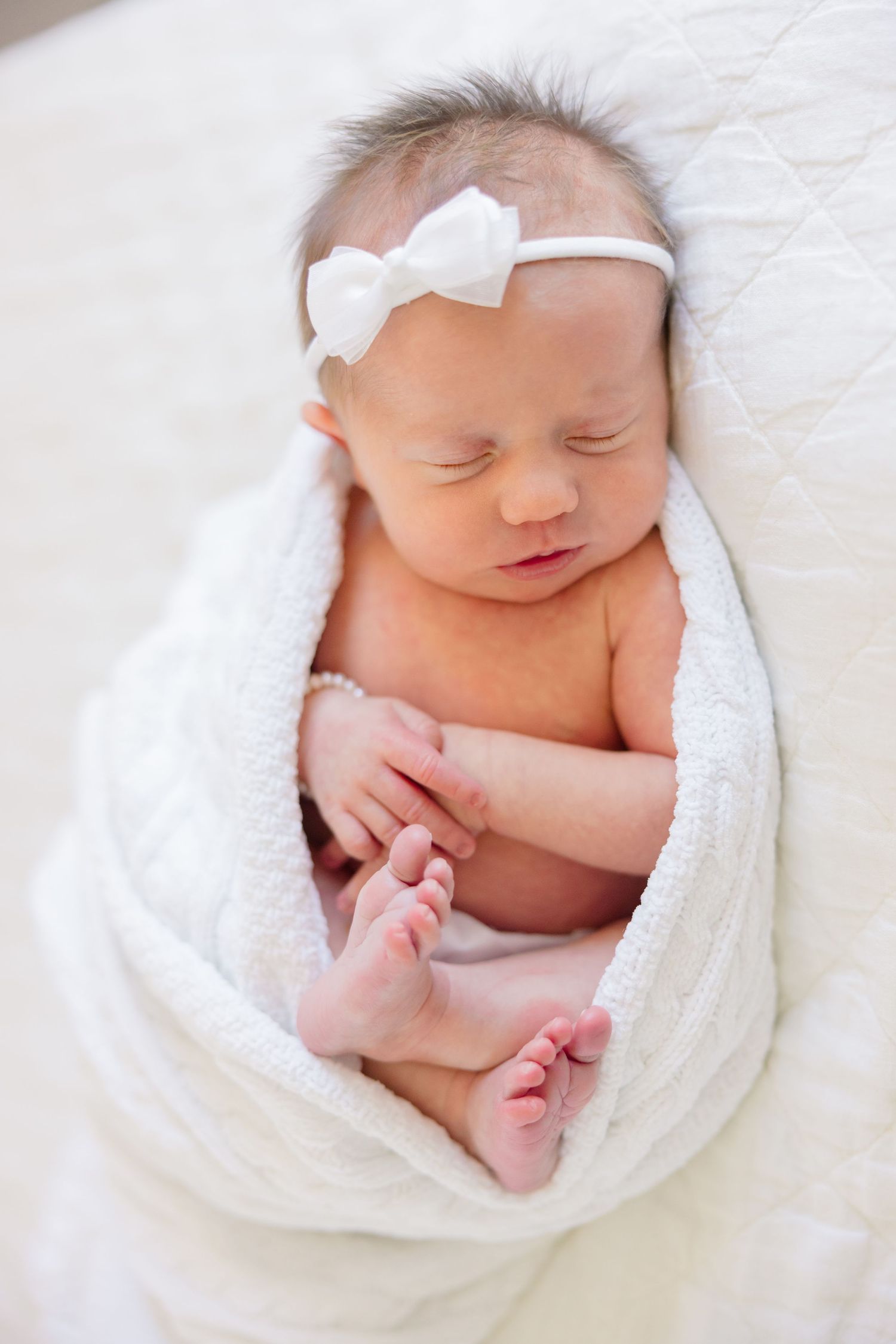 Newborn baby peacefully sleeping while wrapped in soft white blanket in series of gentle poses.