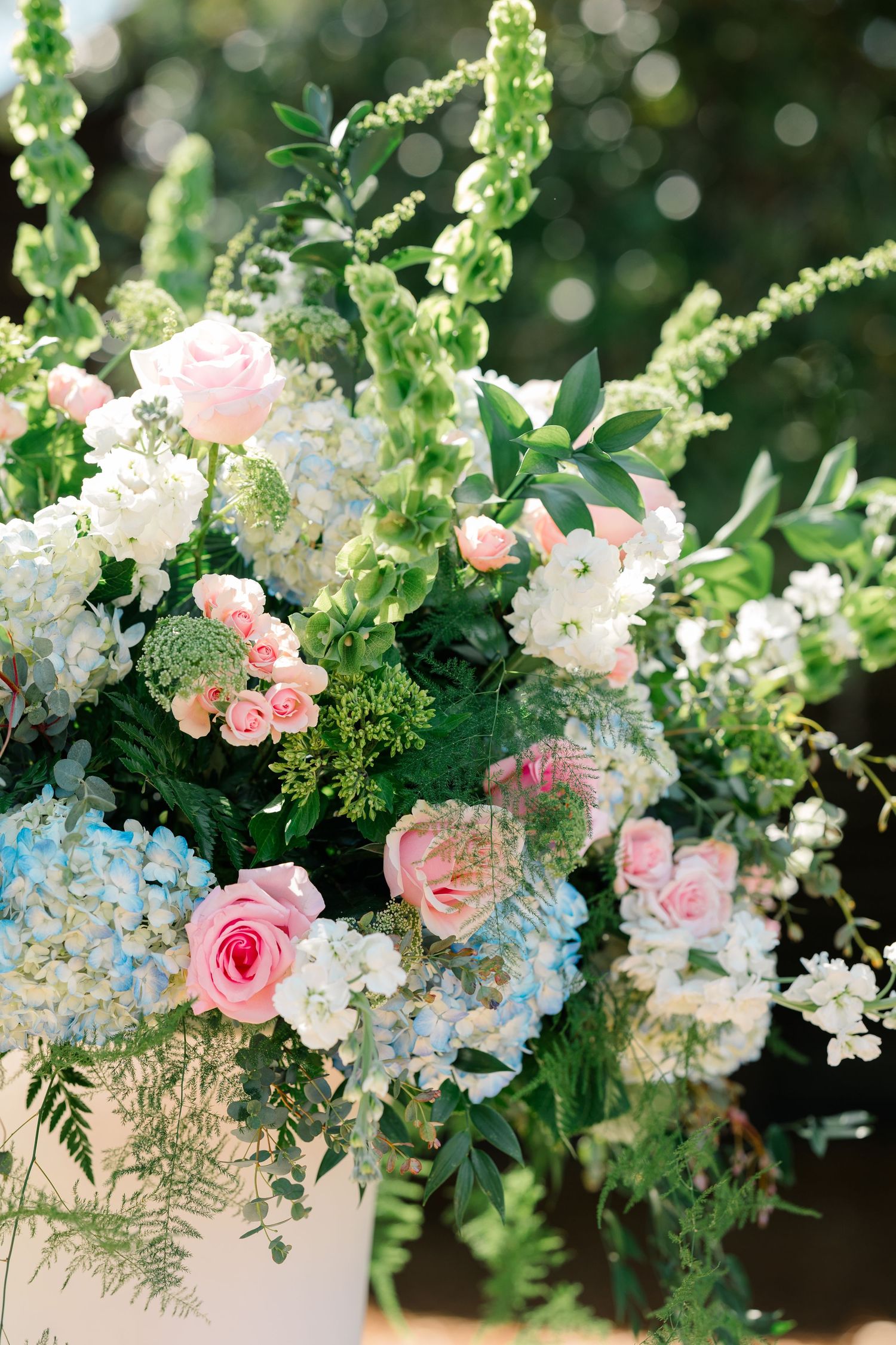 Elegant floral arrangement featuring pink roses, white blooms, and light blue hydrangeas in a white container.