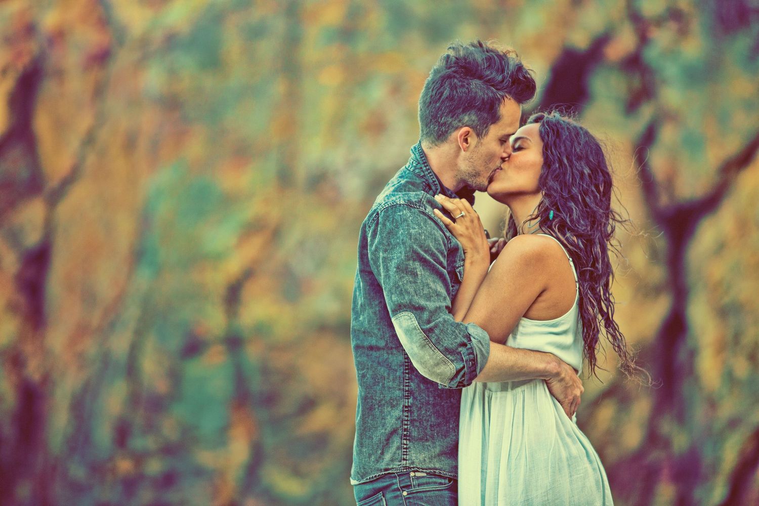 Romantic couple sharing a tender kiss outdoors, surrounded by colorful autumn foliage in warm tones.
