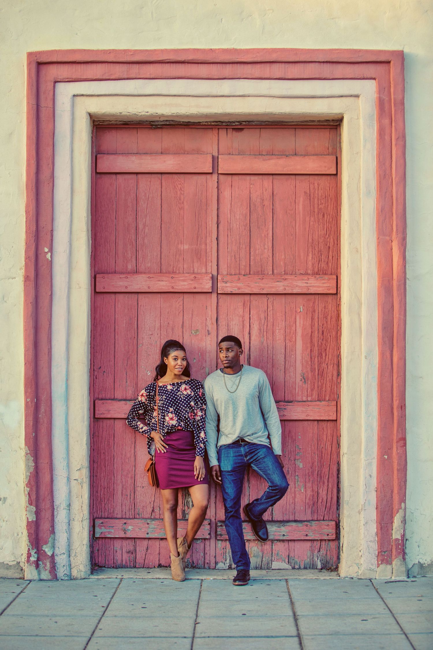 Stylish couple posing in front of a rustic red wooden door on a cobblestone street.